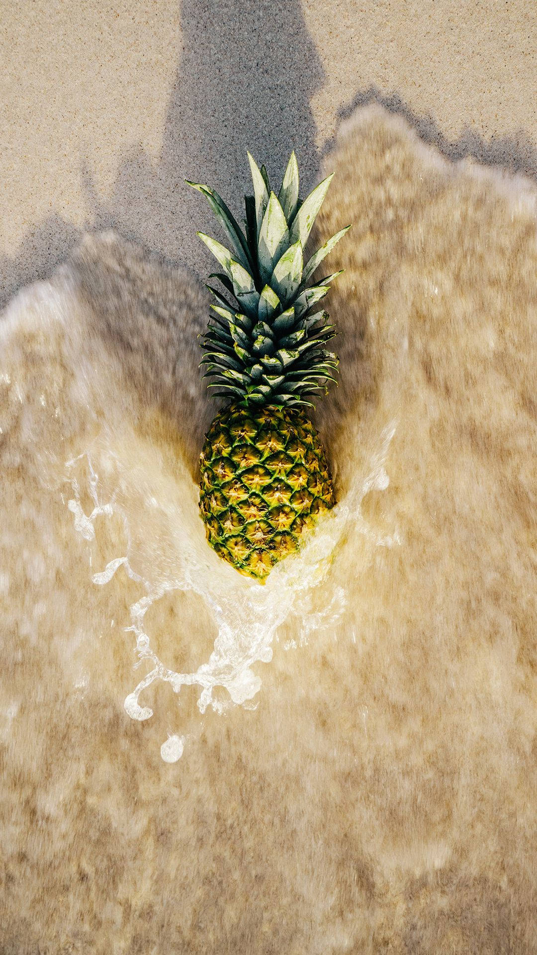 Pineapple 桌布 壁紙 — 一個鳳梨放在沙灘上，溫柔的海浪在它的底部濺起水花。