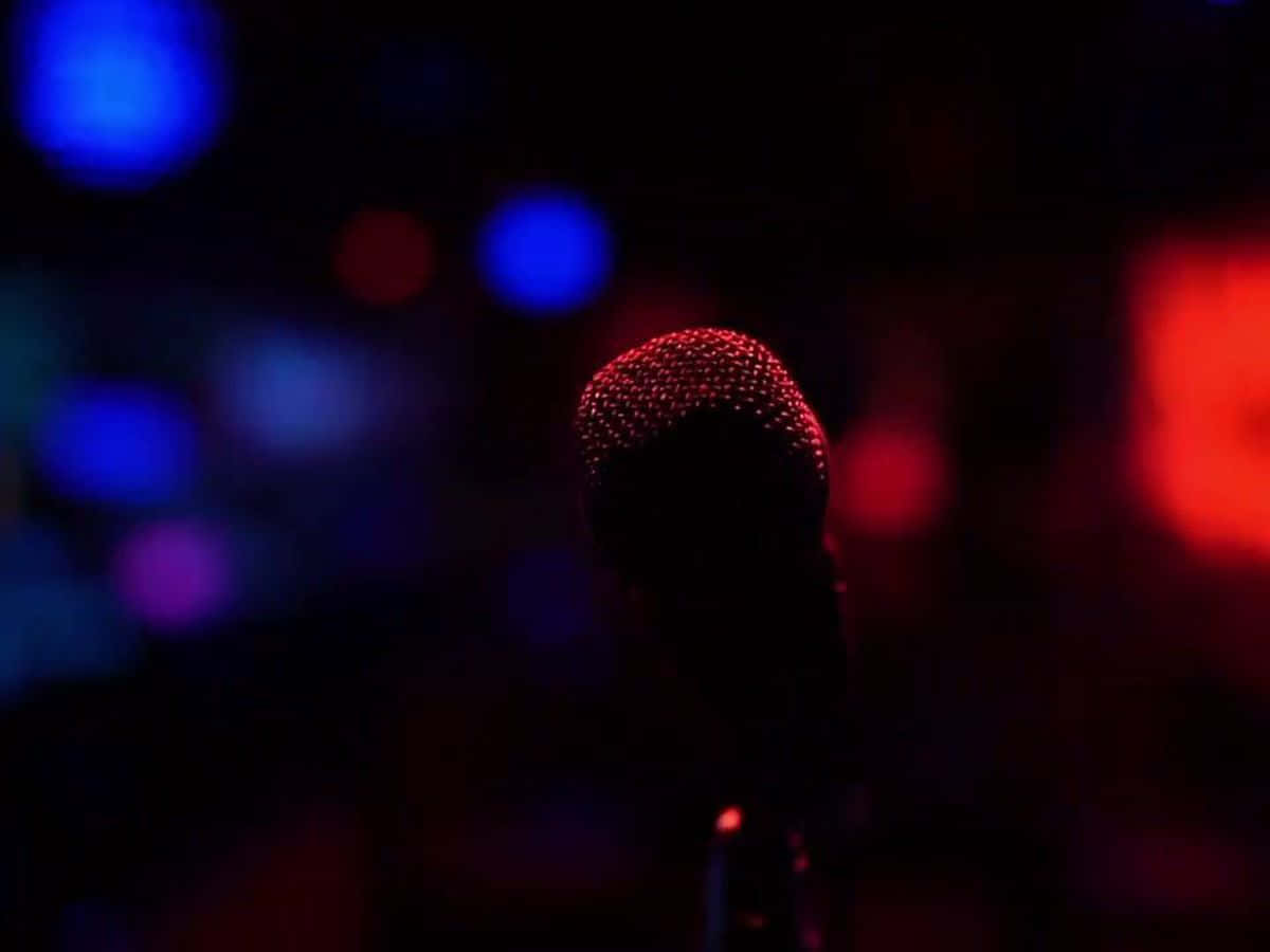Karaoke 桌布 壁紙 — 一個麥克風剪影在模糊的藍色和紅色舞台燈光的黑暗背景下發出紅光。