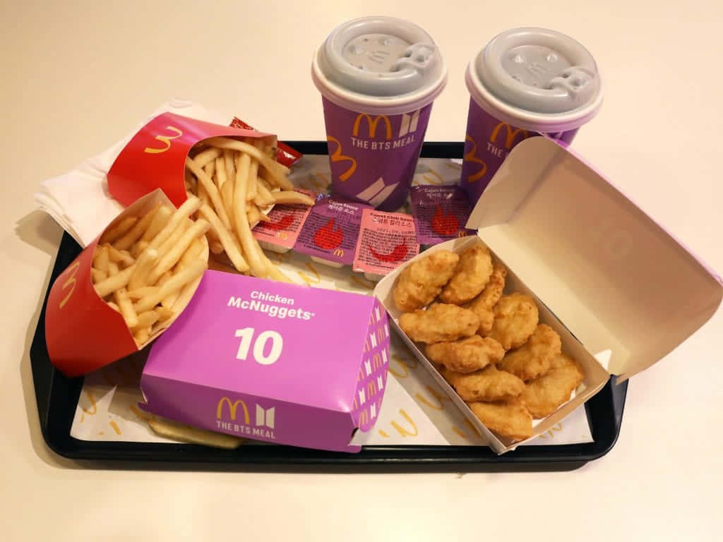 Bts Mac 桌布 壁紙 — 一個麥當勞BTS Meal托盤，上面有紫色雞肉麥克雞塊、薯條和兩杯飲料，在明亮燈光下。