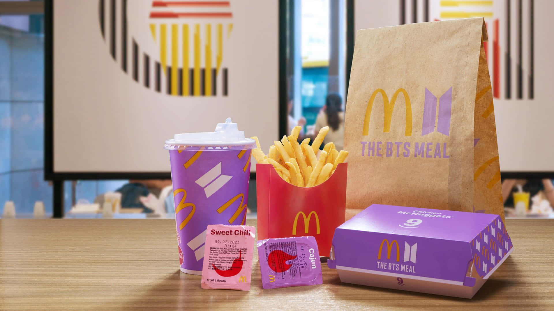Bts Mac 桌布 壁紙 — 一個麥當勞BTS餐，包括紫色包裝的薯條、醬汁和一個品牌袋，擺放在木桌上。