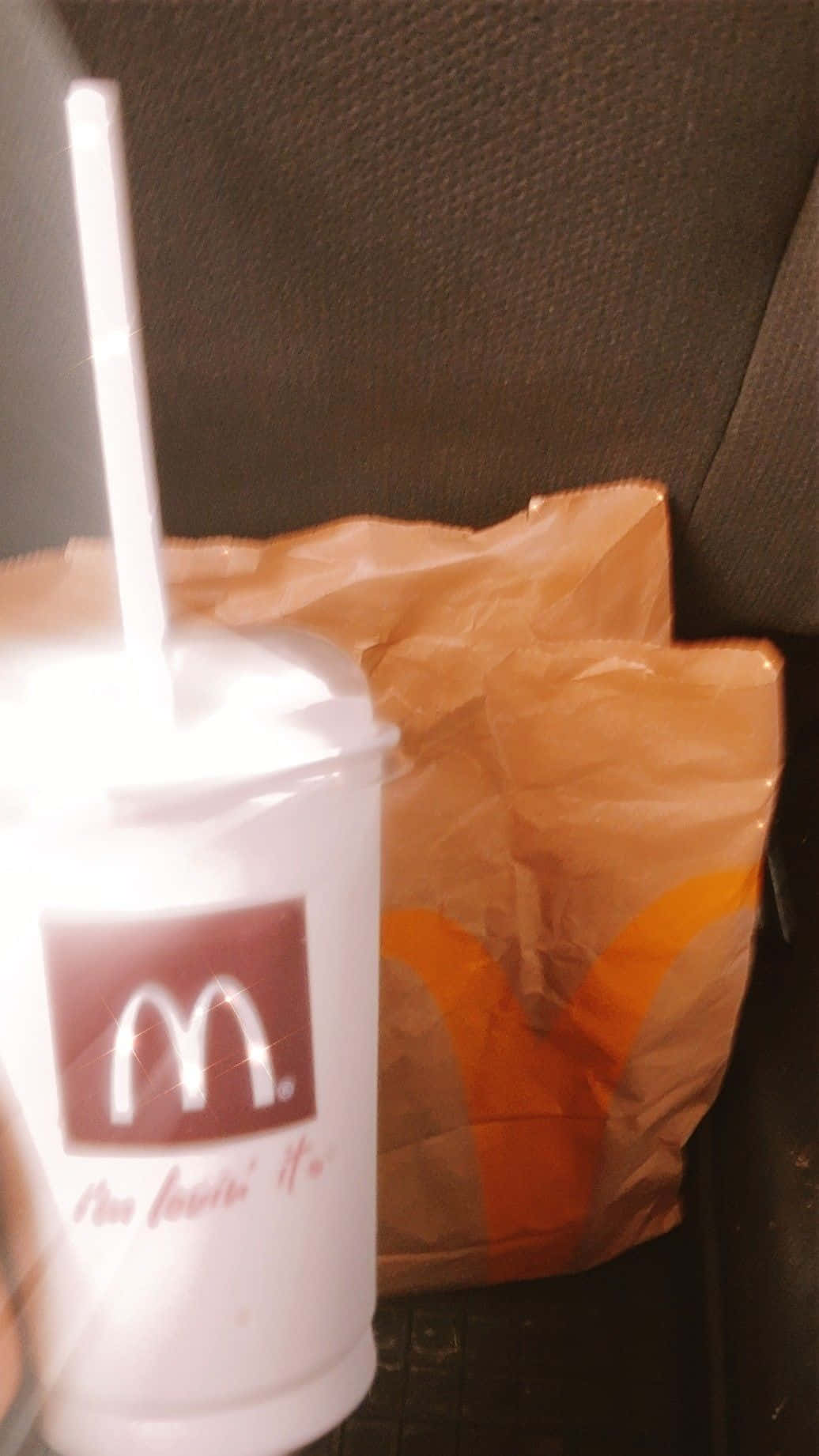 麥當勞 桌布 壁紙 — 一個麥當勞飲料杯連吸管放在車座上，旁邊有一個皺巴巴的紙袋。