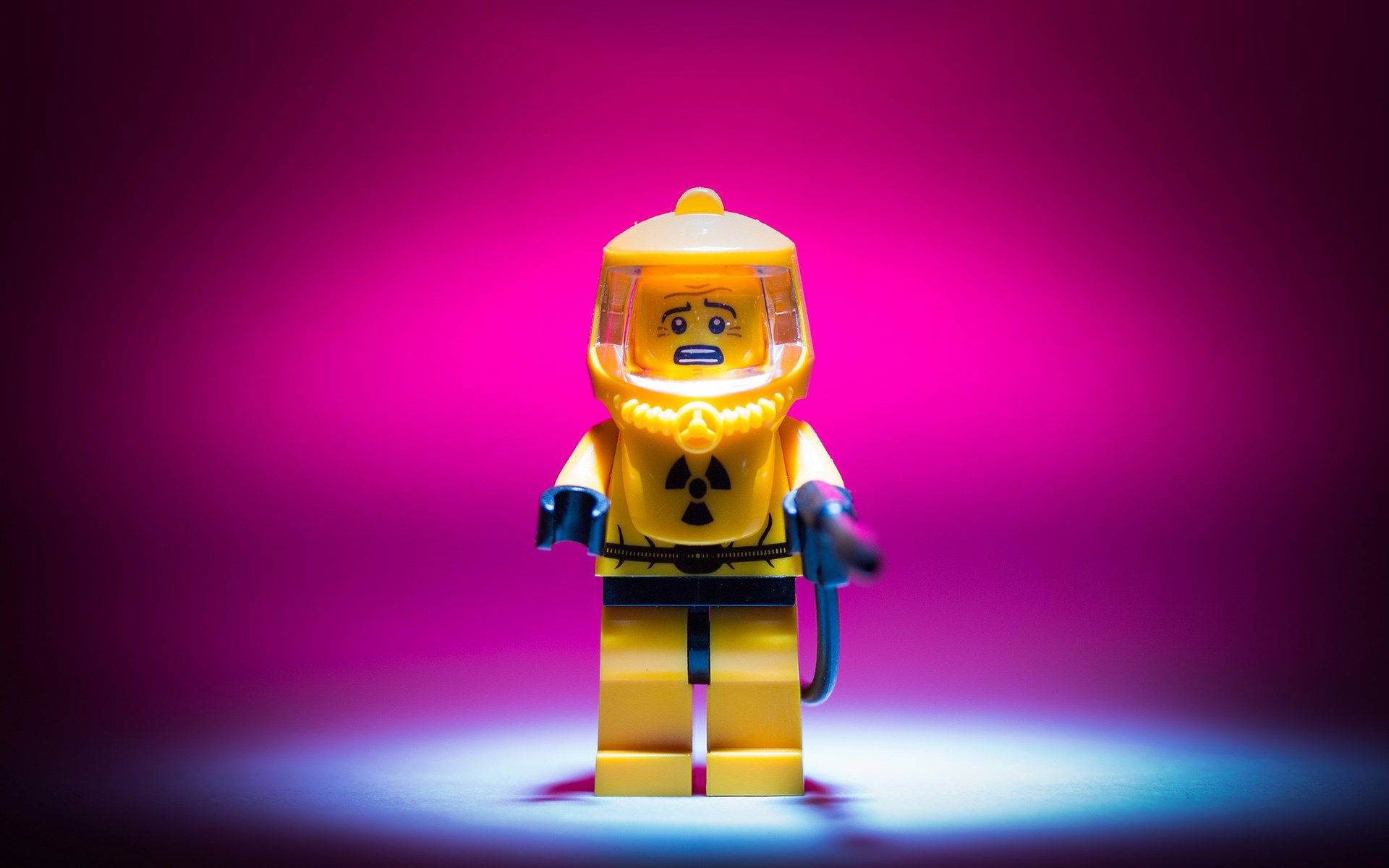 樂高 桌布 壁紙 — 一個黃色LEGO迷你人偶穿著防護衣，站在聚光燈下，背景是充滿活力的洋紅色漸變色。
