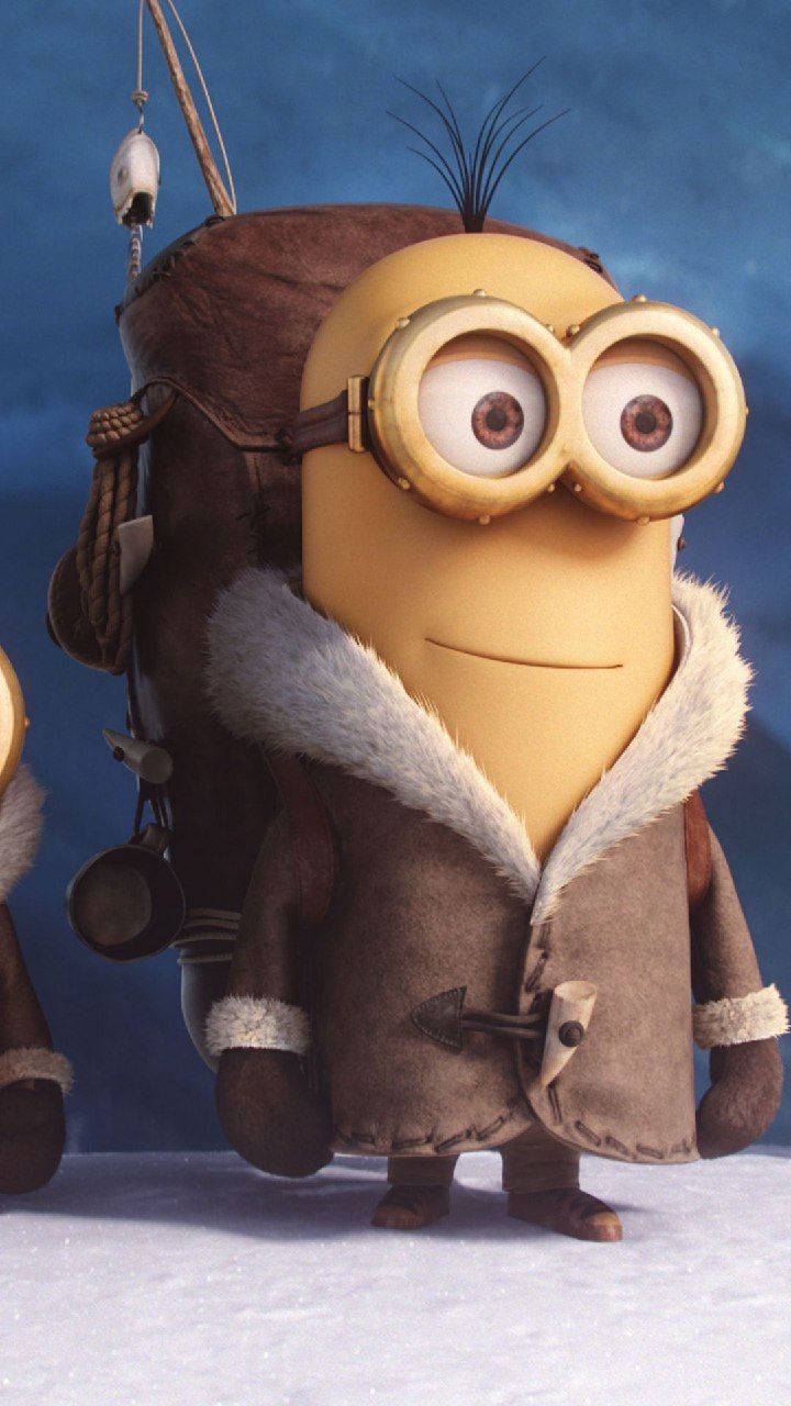 小小兵 桌布 壁紙 — 一個黃色Minion穿著棕色毛領外套和護目鏡，站在雪地上，背景是藍色。
