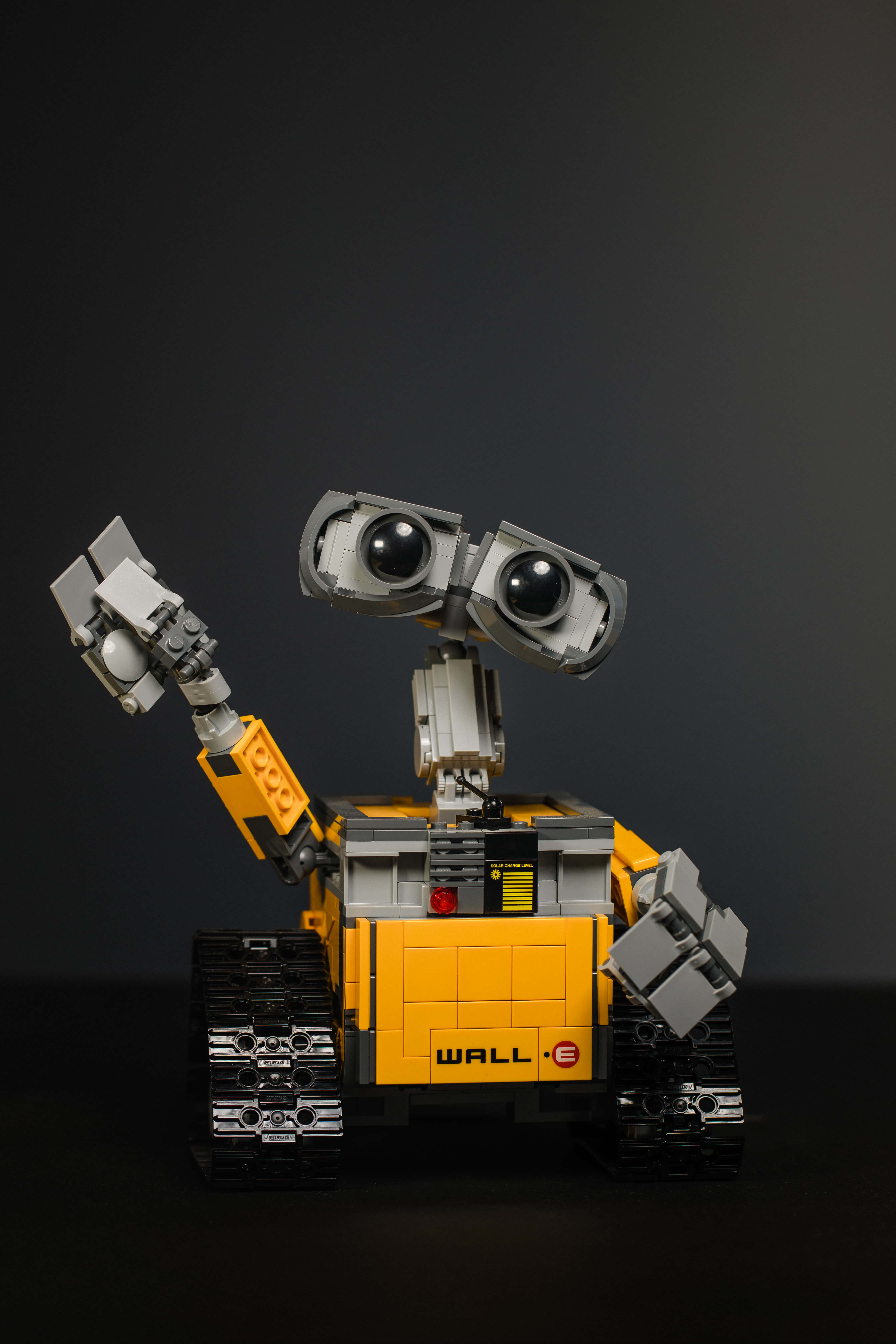 機器人 桌布 壁紙 — 一個黃色和灰色的LEGO WALL-E機器人在深色工作室背景前愉快地揮手。