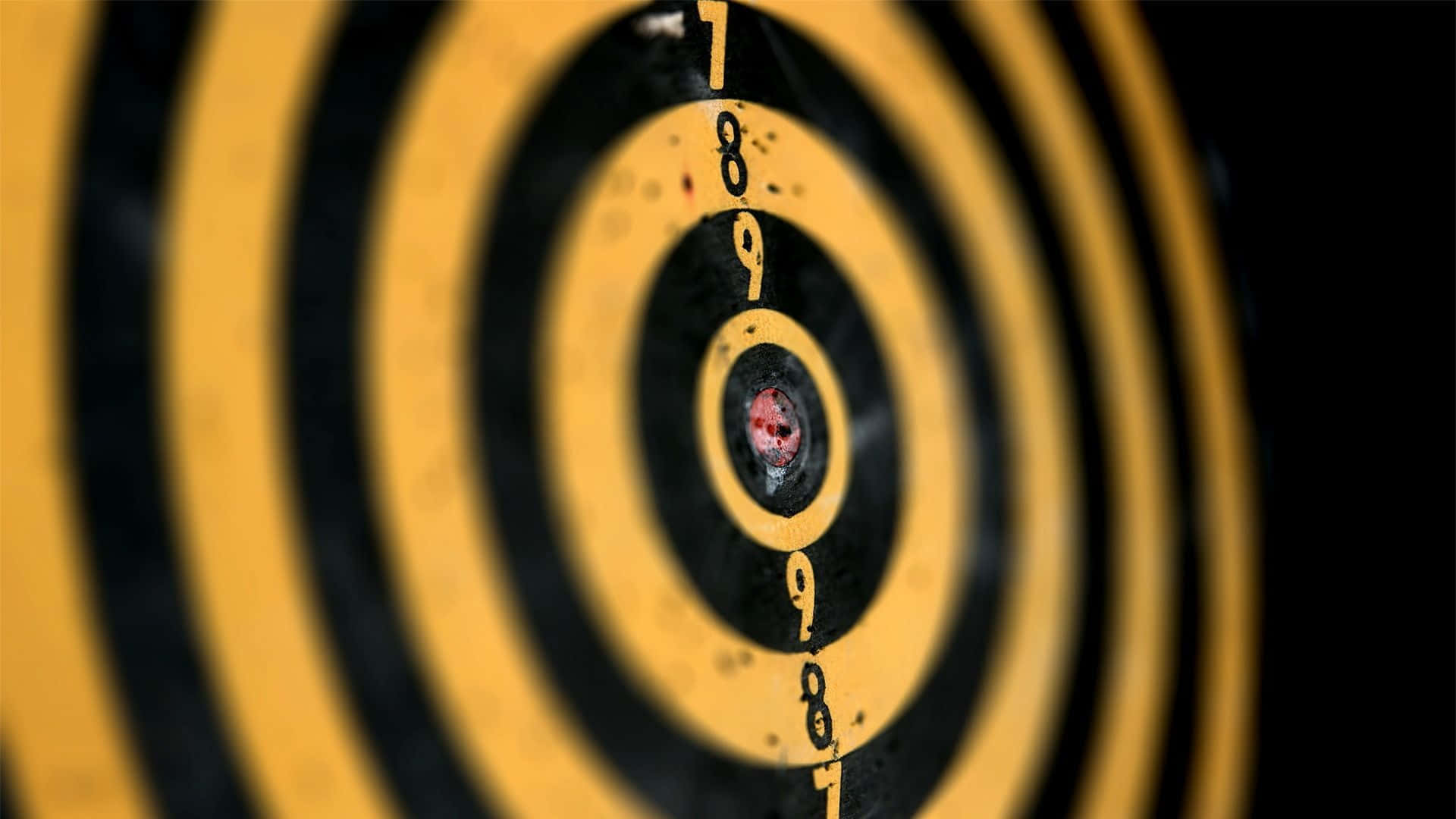 Shooting 桌布 壁紙 — 一個黃色和黑色飛鏢靶的特寫，中央靶心插著一支紅色飛鏢。