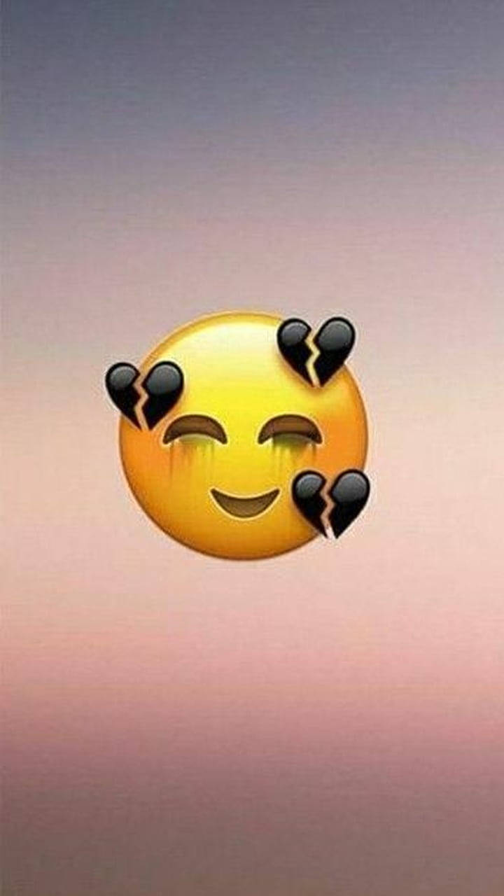 Black Emoji 桌布 壁紙 — 一個黃色哭泣的表情符號帶有破碎的心形圖標，漂浮在柔和的粉紅色和紫色漸變天空上。