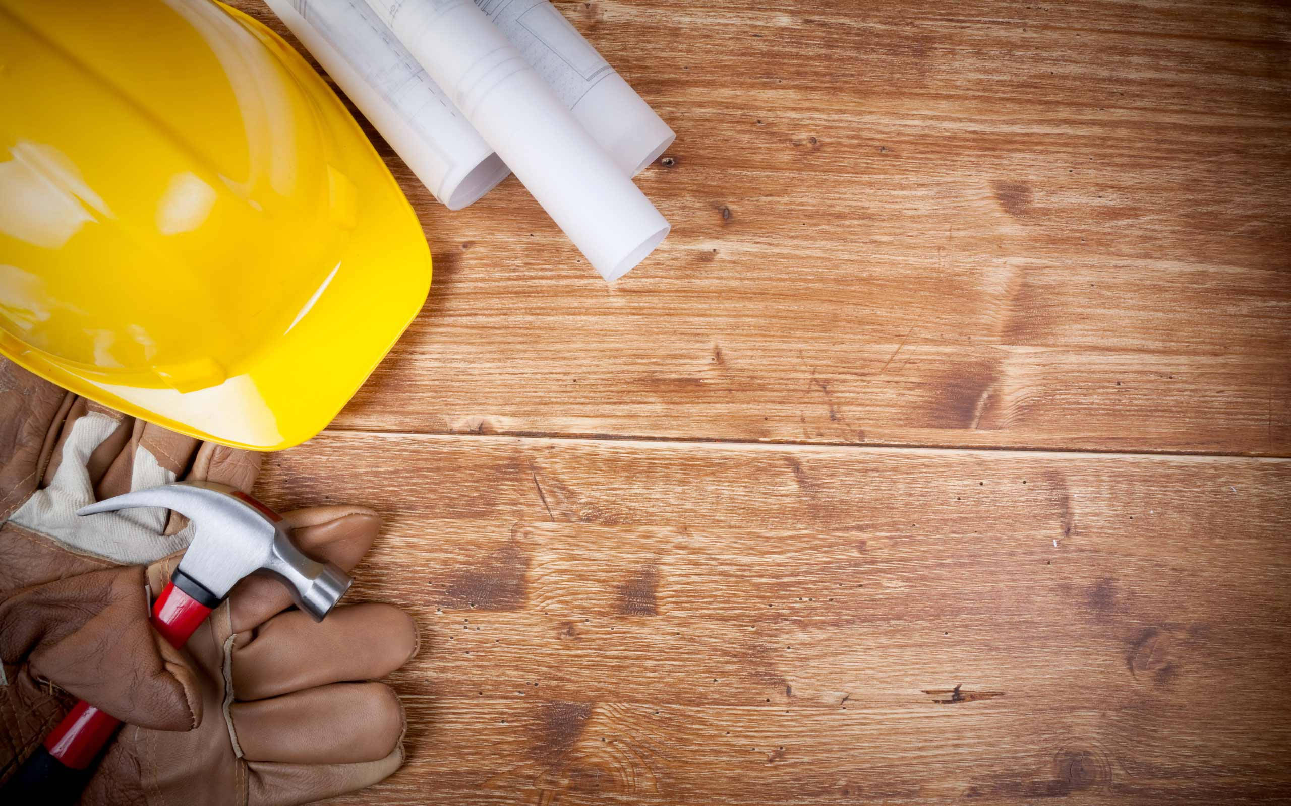 木紋 桌布 壁紙 — 一個黃色安全帽、鎚子和工作手套放在粗糙木製工作台上的捲起藍圖旁邊。