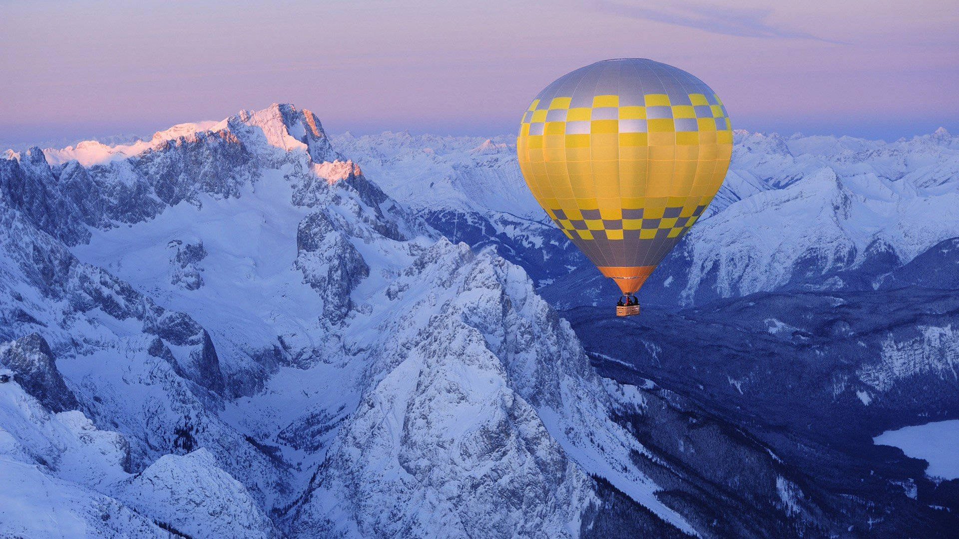 Hot Air Balloon 桌布 壁紙 — 一個黃色格子熱氣球在暮色中寧靜地飄浮在積雪的山峰之上。