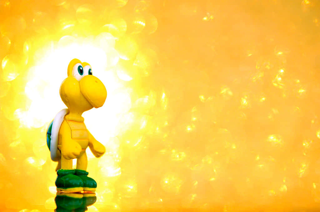 Koopa Troopa 桌布 壁紙 — 一個黃色的Koopa Troopa玩具站在發光的金色散景背景前，帶有柔和的光線反射。