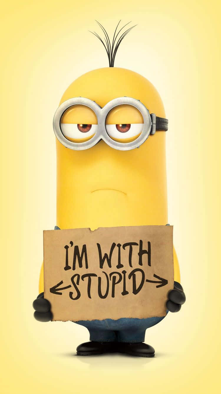 搞笑 桌布 壁紙 — 一個黃色的Minion，有一束頭髮和護目鏡，在淡黃色背景前舉著一塊寫著「I'M WITH STUPID」的紙板牌。