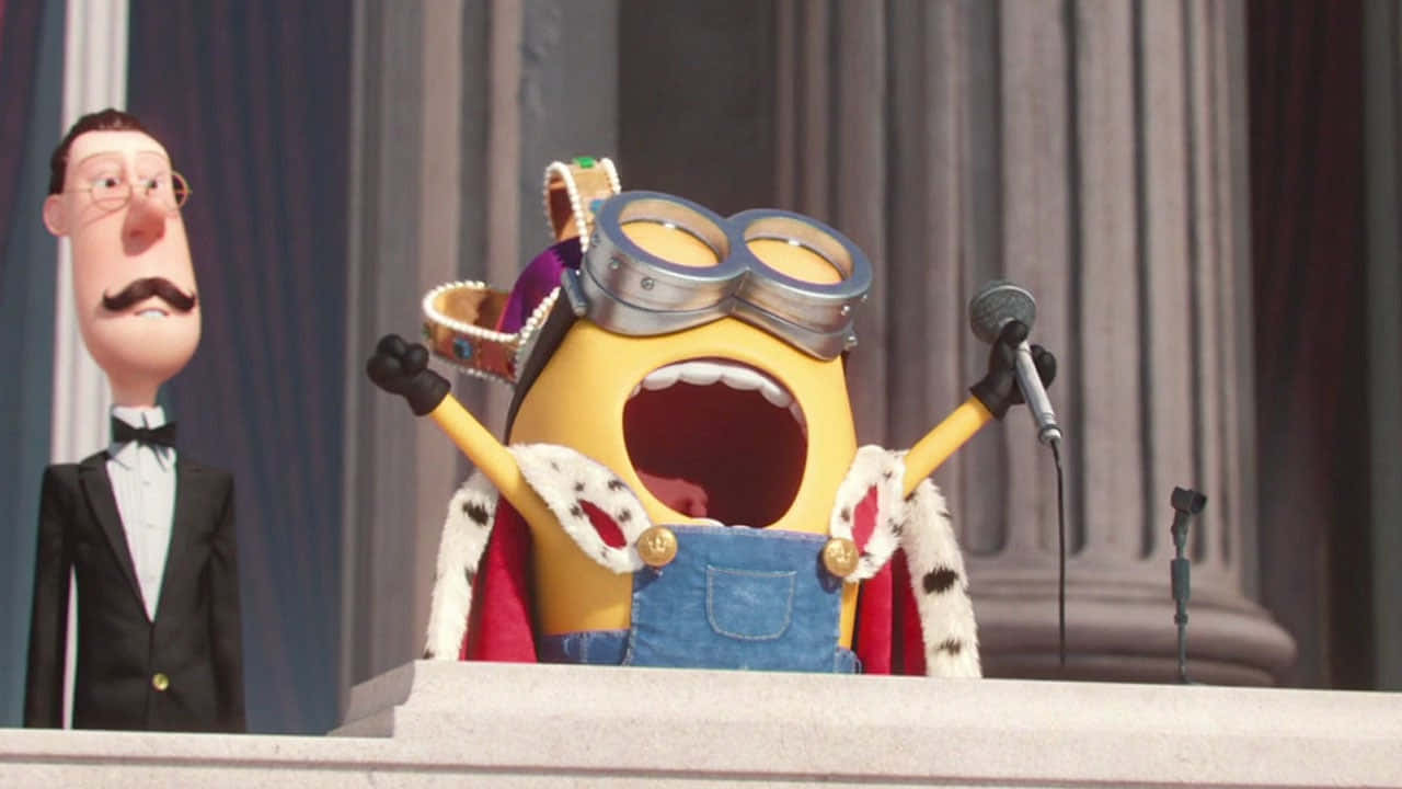 小黃人 桌布 壁紙 — 一個黃色的Minion穿著皇室服裝對著麥克風大叫，而一個穿著燕尾服的男人在旁邊看著。