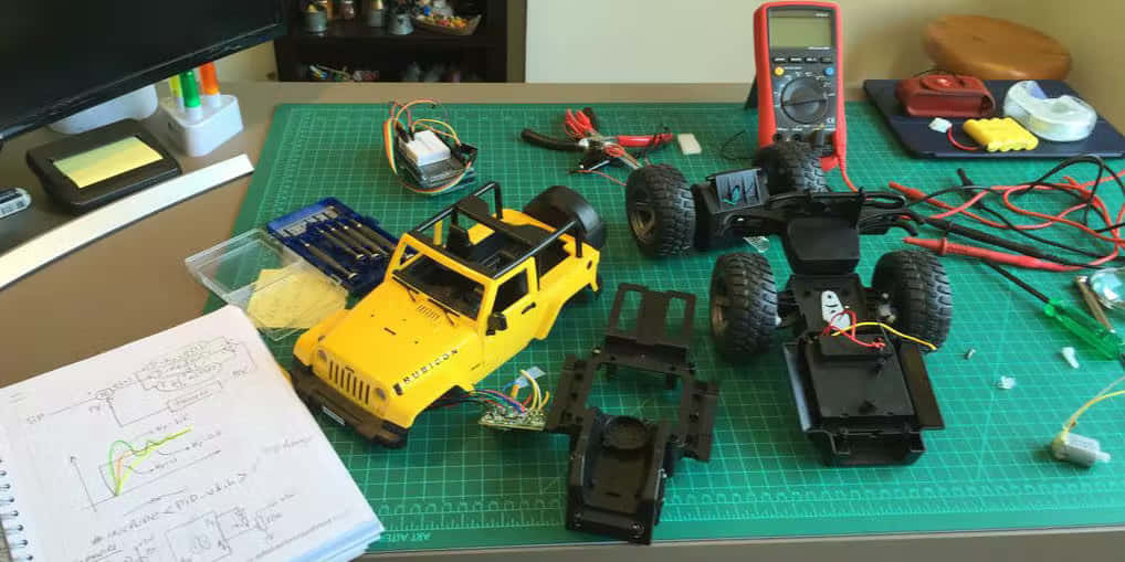Rc Cars 桌布 壁紙 — 一個黃色遙控吉普車模型正在綠色網格墊上建造，周圍有工具和電子零件。
