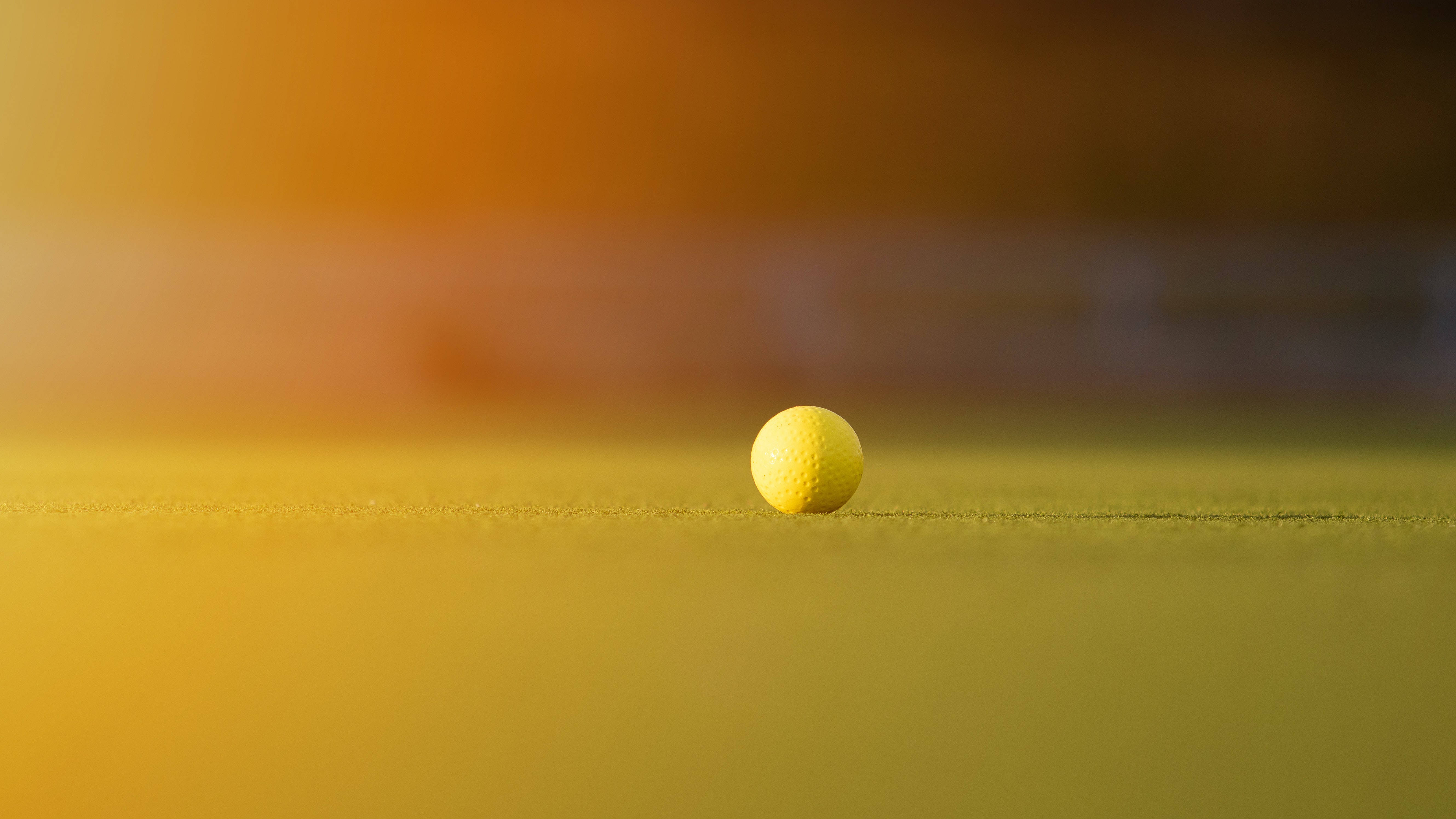 4K Golf 桌布 壁紙 — 一個黃色高爾夫球在溫暖的金色日落餘暉下，靜置於充滿活力的綠色球場上。