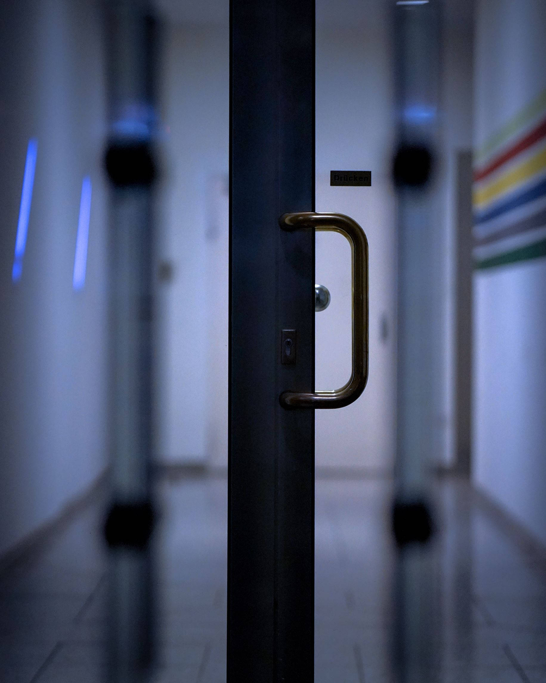 Door 桌布 壁紙 — 一個黃銅門把手的特寫，在一條昏暗走廊的深色門上，背景有模糊的藍色燈光和彩色條紋。