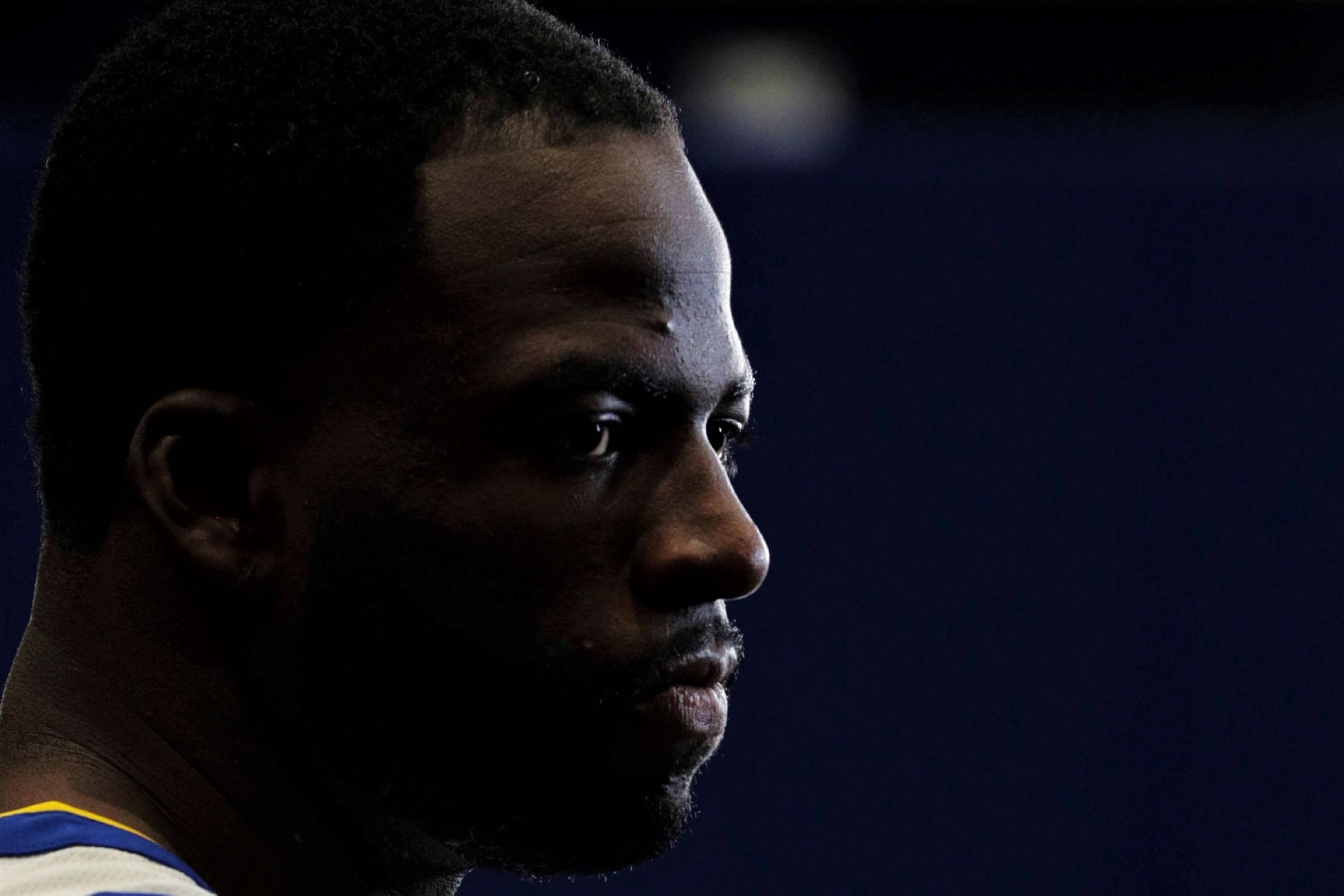 Draymond Green 桌布 壁紙 — 一個黑人男子的側面特寫肖像，在深藍色背景下戲劇性地打光，傳達出強烈的專注。