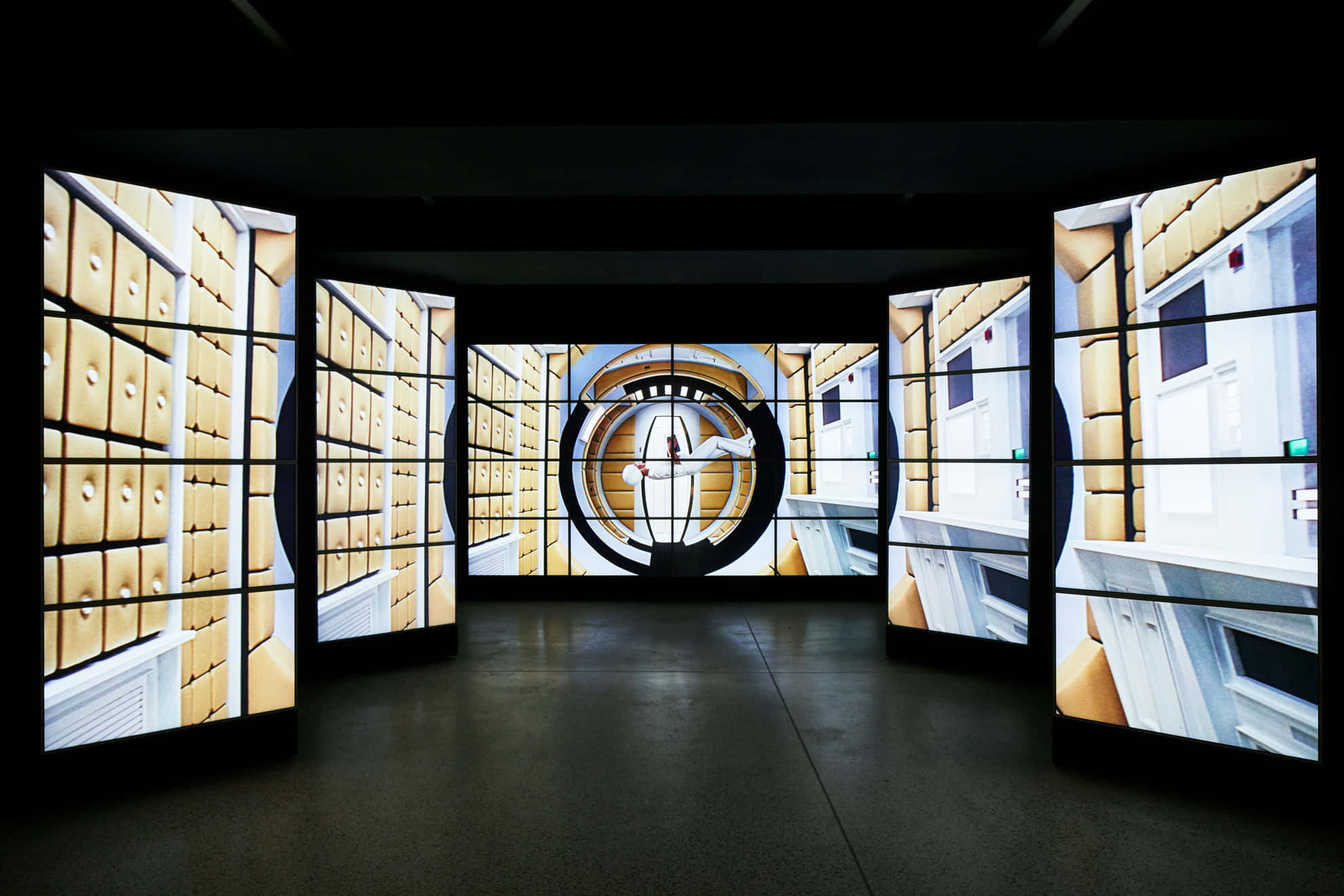 Exhibition 桌布 壁紙 — 一個黑暗的房間設有彎曲的數位螢幕，顯示重複的黃色文件櫃和白色門的圖案，中央有一個圓形投影。