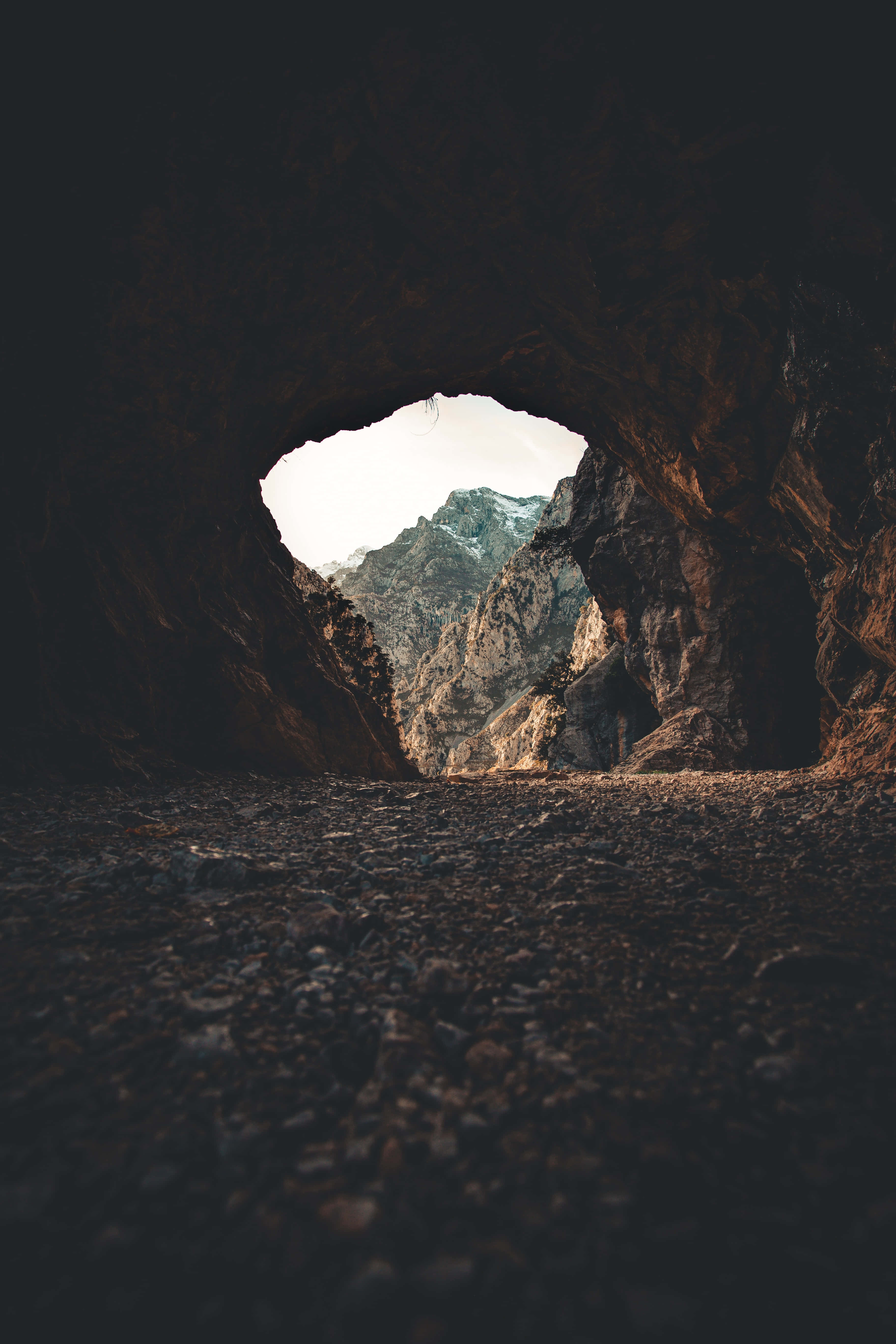 Cave 桌布 壁紙 — 一個黑暗的洞穴入口框住了蒼白天空下崎嶇的積雪山脈的明亮景色。