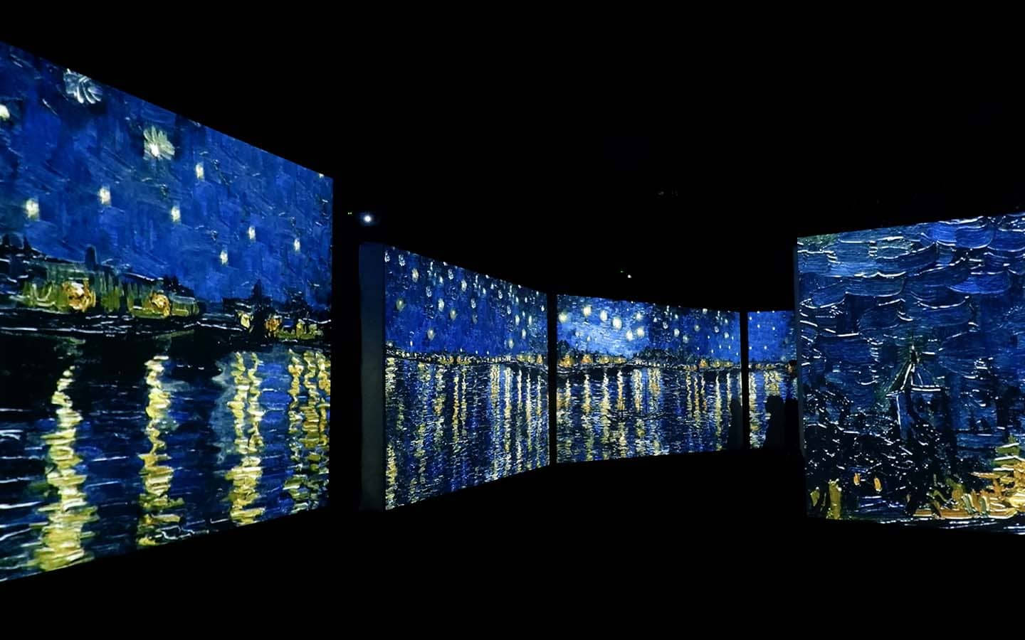 藝術 桌布 壁紙 — 一個黑暗的畫廊展示了梵谷《星夜》的沉浸式數位投影，鮮豔的藍色和發光的黃色在水面上反射。