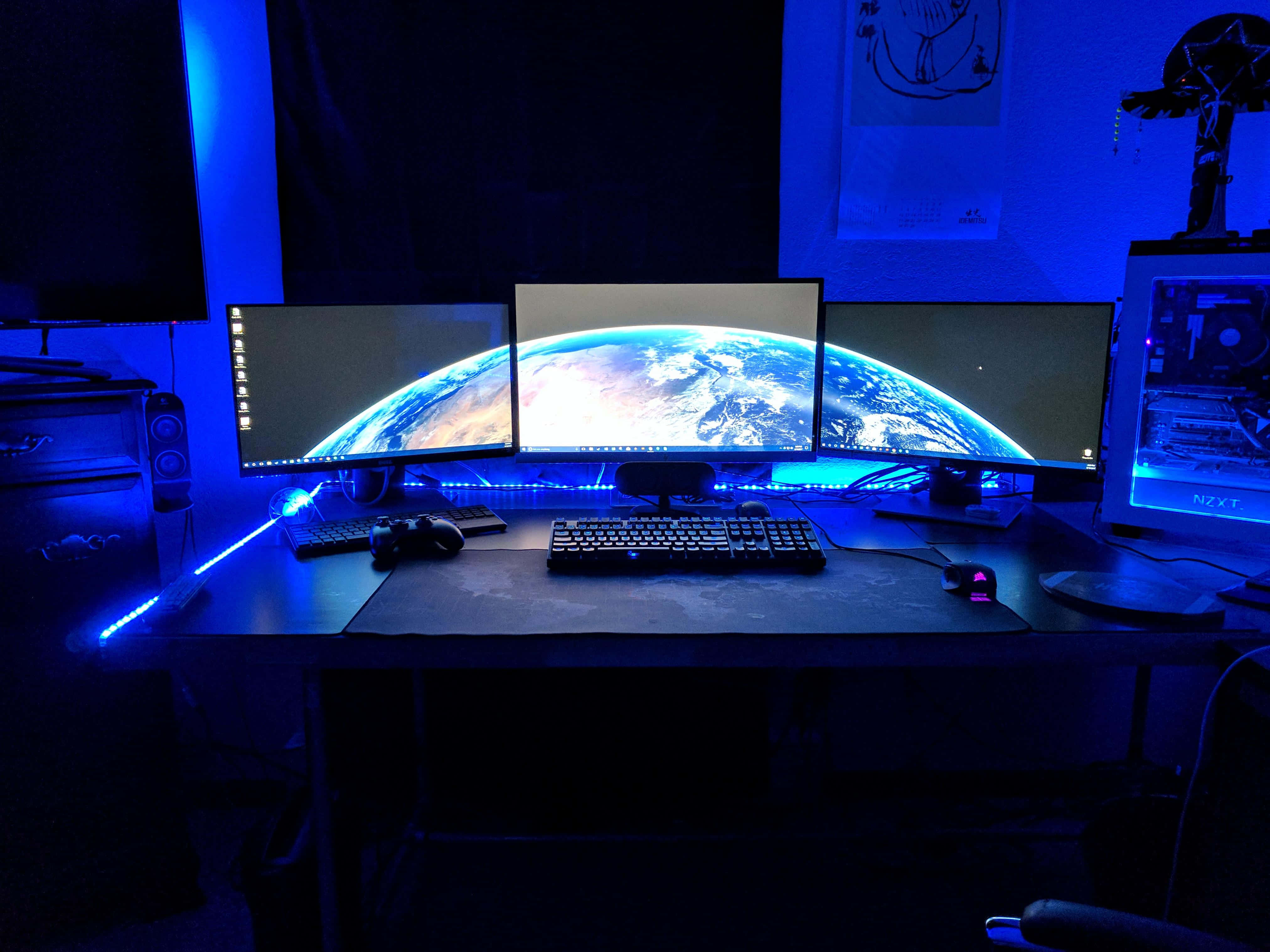Monitor 桌布 壁紙 — 一個黑暗的遊戲設置，沐浴在藍色LED燈光中，三個顯示器顯示彎曲的地球桌布。