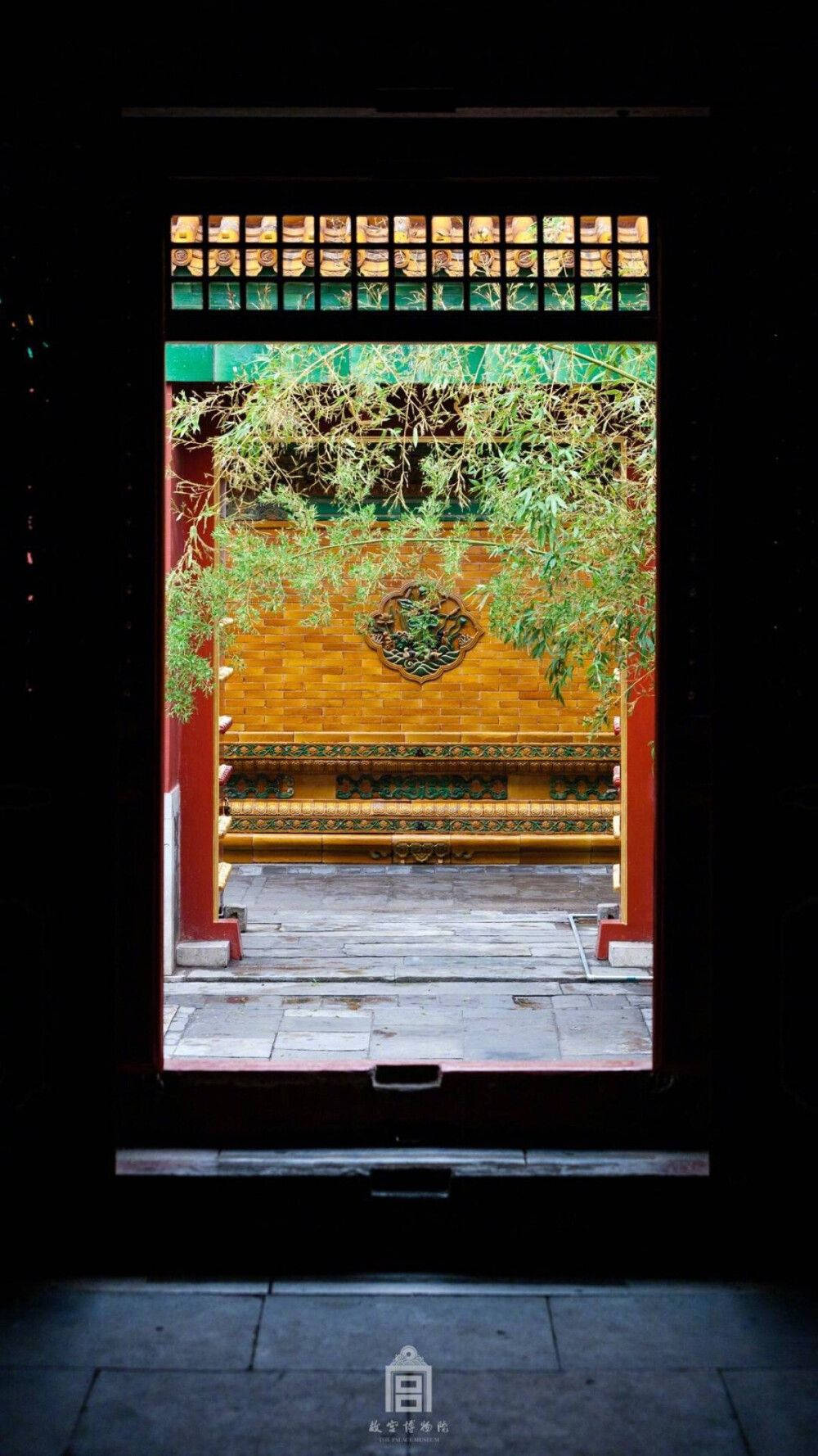攝影 桌布 壁紙 — 一個黑暗的門口框住了一個充滿活力的庭院，有金色的牆壁、紅色的柱子和優雅垂掛的綠色藤蔓。