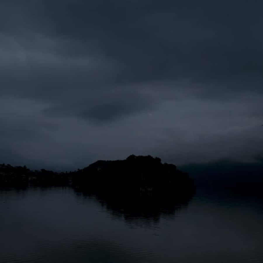Dark Island 桌布 壁紙 — 一個黑暗風暴的湖泊在沉重的灰色天空下映照出一個剪影島嶼。