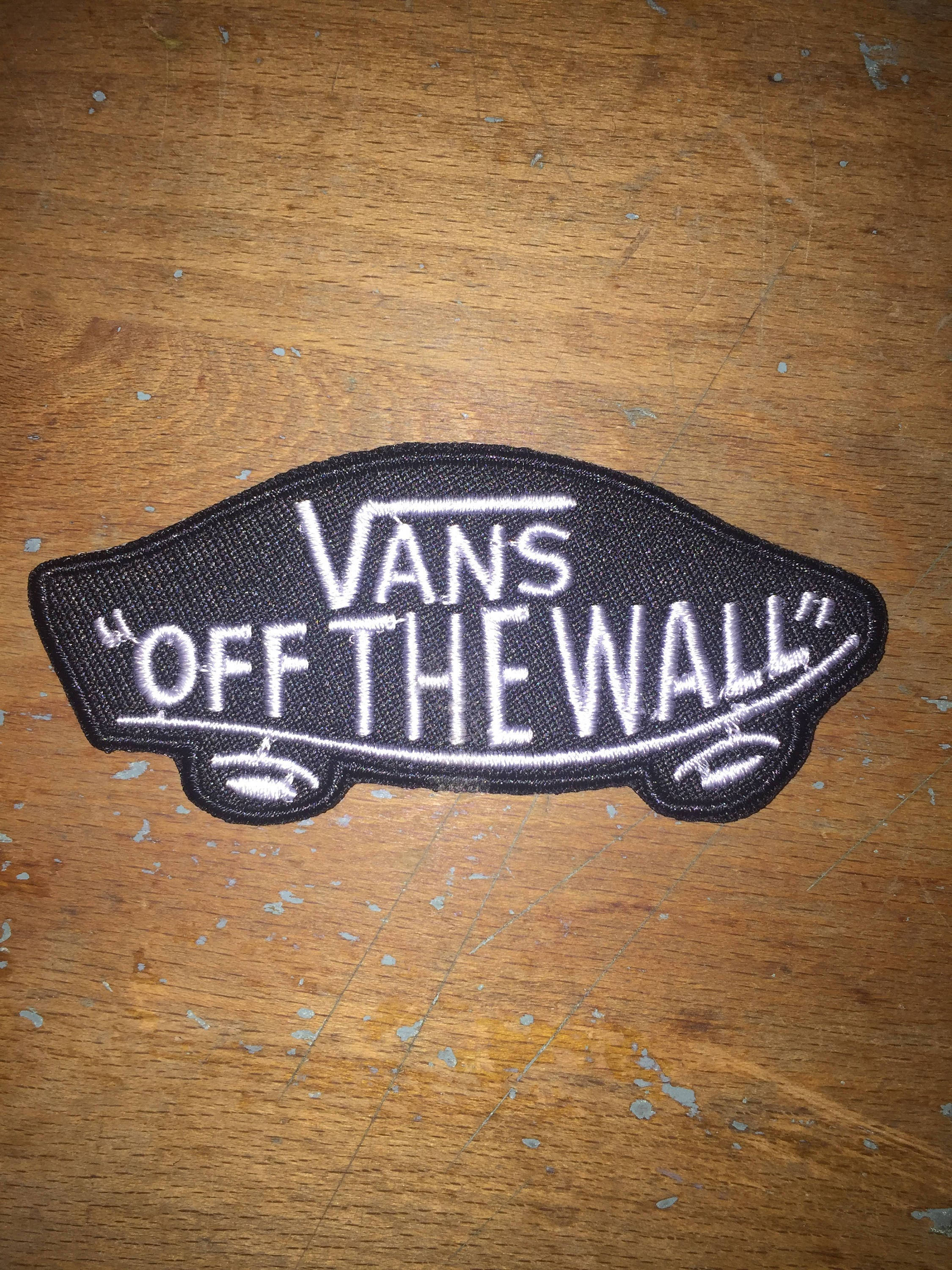 Vans Off The Wall 桌布 壁紙 — 一個黑白Vans 'Off The Wall' 布章放在一塊有明顯刮痕和油漆剝落的風化木質表面上。
