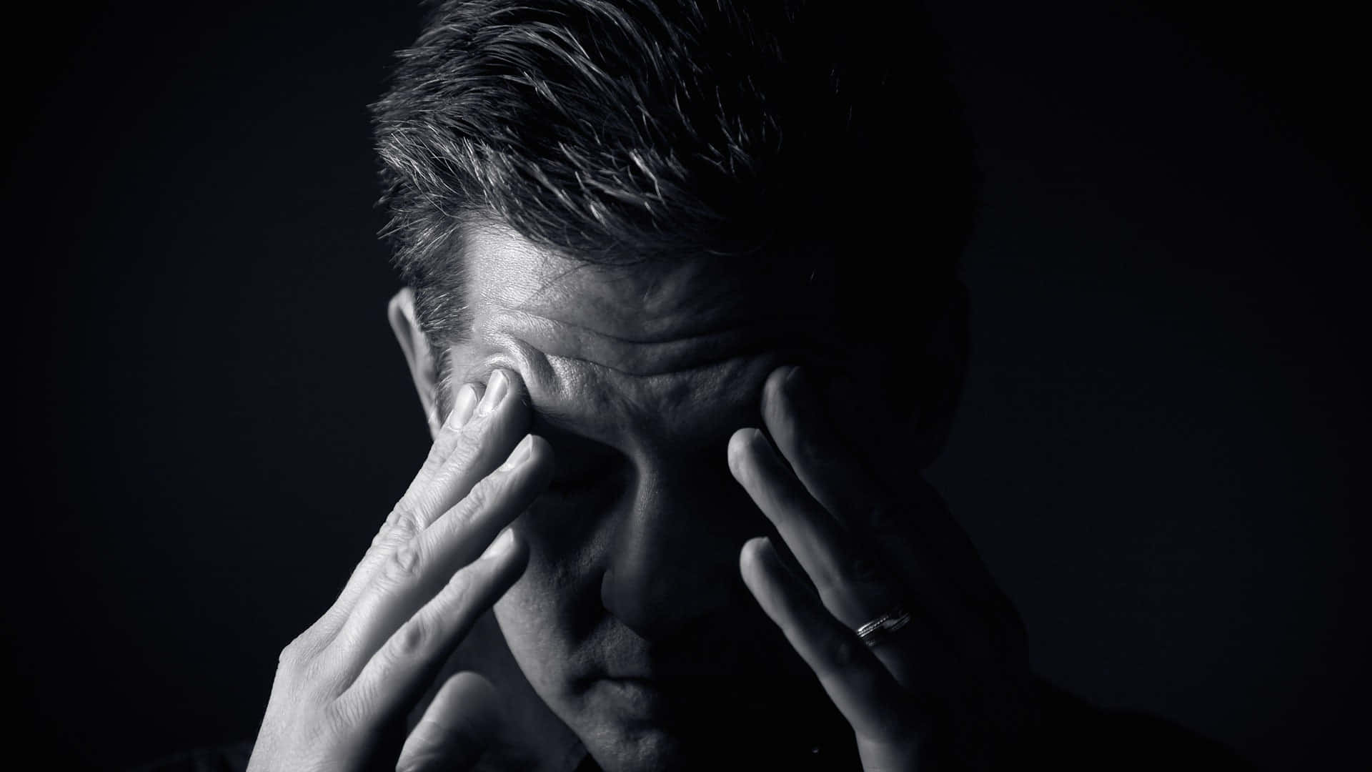 Depressed 桌布 壁紙 — 一個黑白人像的男子在深色背景前將雙手按在太陽穴上，傳達出強烈的壓力或疲憊。