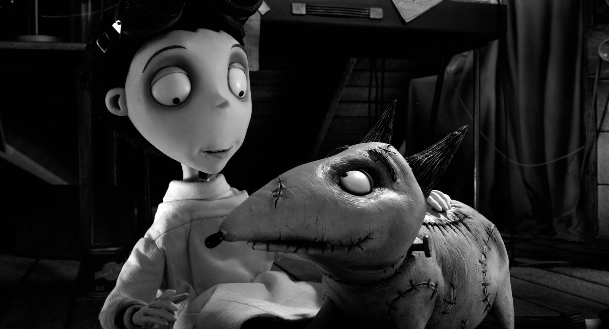 Frankenweenie 桌布 壁紙 — 一個黑白動畫場景顯示，在一個光線昏暗的房間裡，一個年輕女孩溫柔地抱著一個縫合起來、眼睛大大的生物。