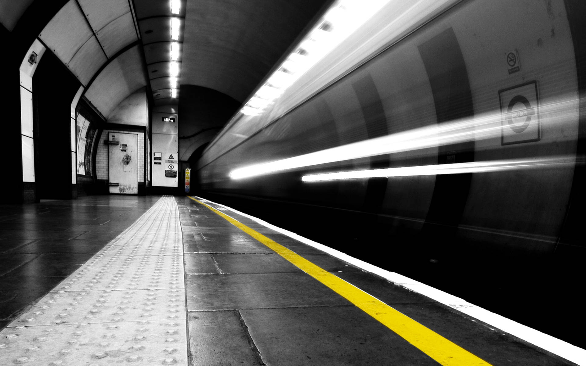 Subway 桌布 壁紙 — 一個黑白地鐵站，一列高速行駛的火車模糊掠過，由一條鮮黃色的安全線突出顯示。
