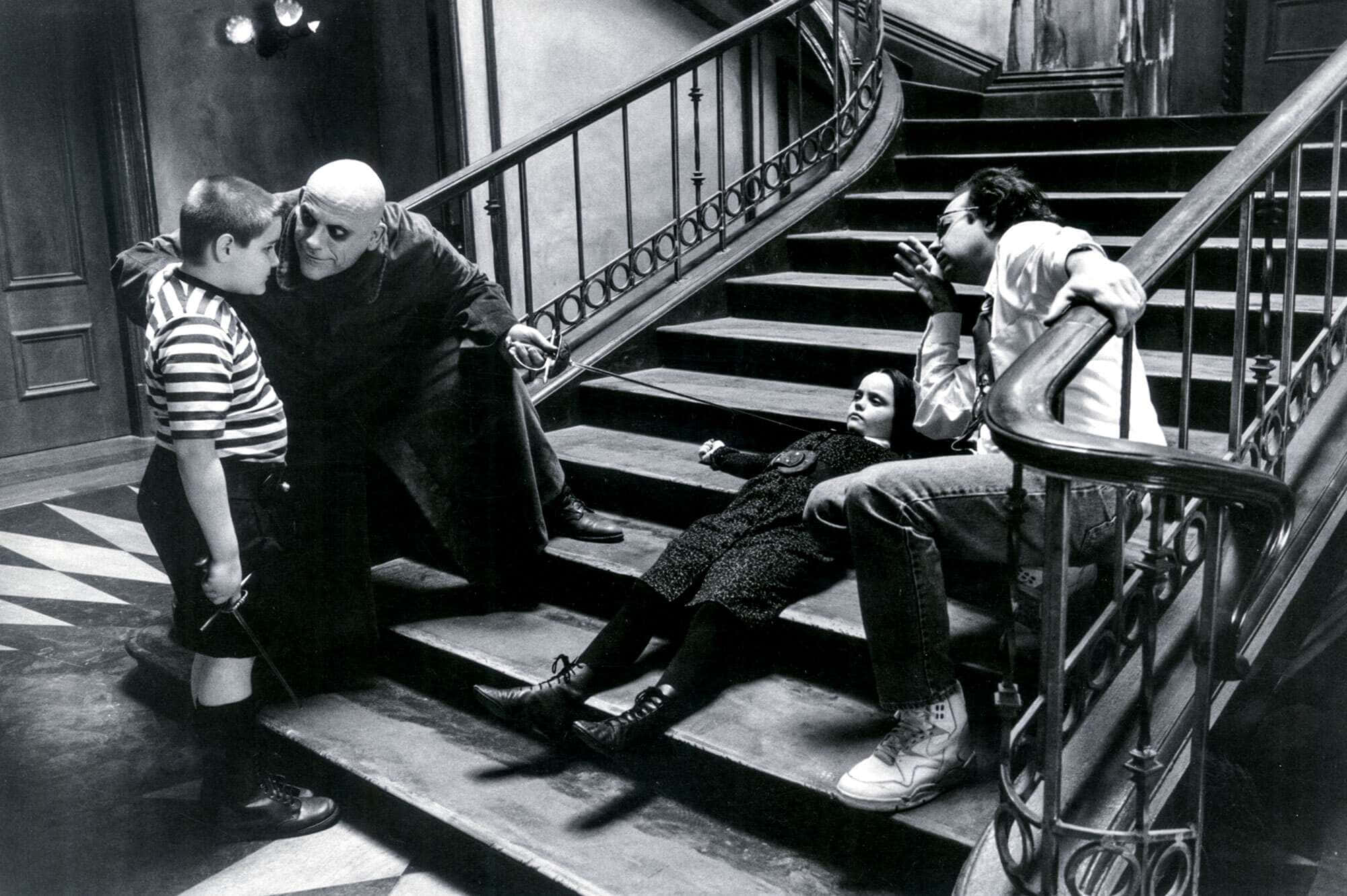 Addams Family 桌布 壁紙 — 一個黑白場景，四個角色在哥德式豪宅的華麗樓梯上，帶有戲劇性的燈光。