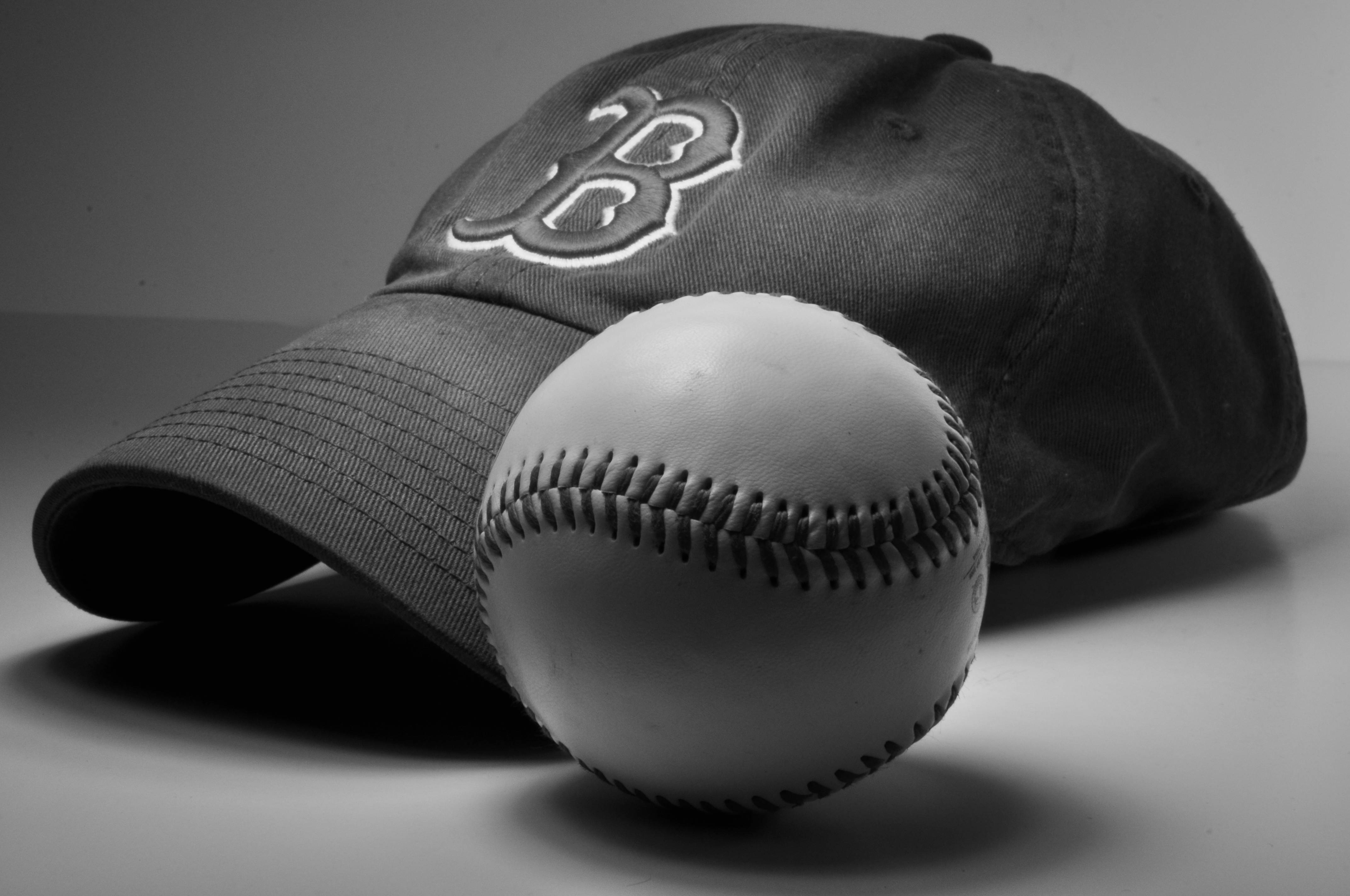 Red Sox 桌布 壁紙 — 一個黑白攝影棚拍攝，一個棒球放在一頂帶有縫製 'B' 標誌的棒球帽前面。