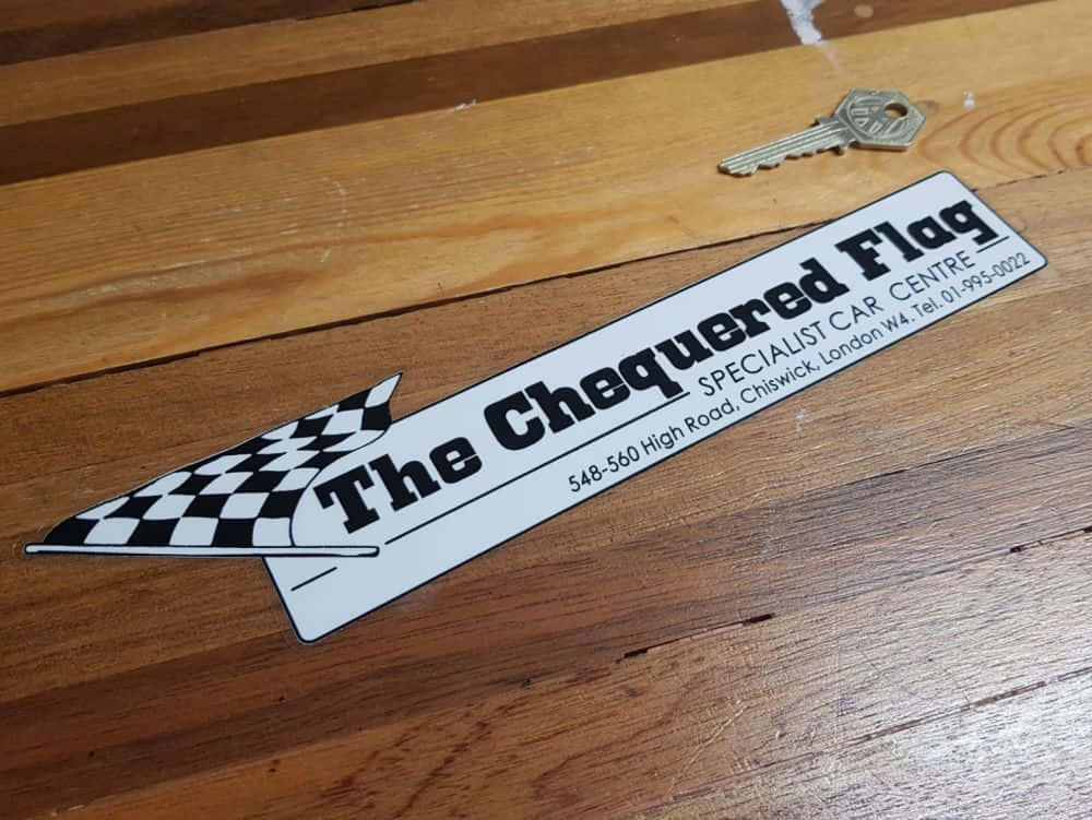 Chequered Flag 桌布 壁紙 — 一個黑白格子旗形狀的招牌，上面寫著「The Chequered Flag Specialist Car Centre」，放在木地板上，旁邊有一把鑰匙。