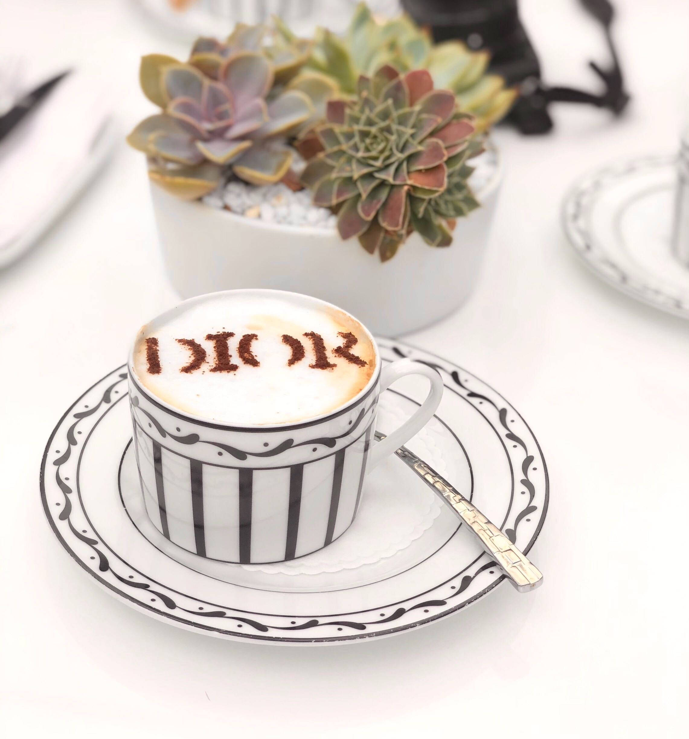 Dior 動態 桌布 壁紙 — 一個黑白條紋杯盛裝著拿鐵，上面有可可粉製成的「I ❤️ K」圖案，旁邊有一盆多肉植物在白色桌子上。
