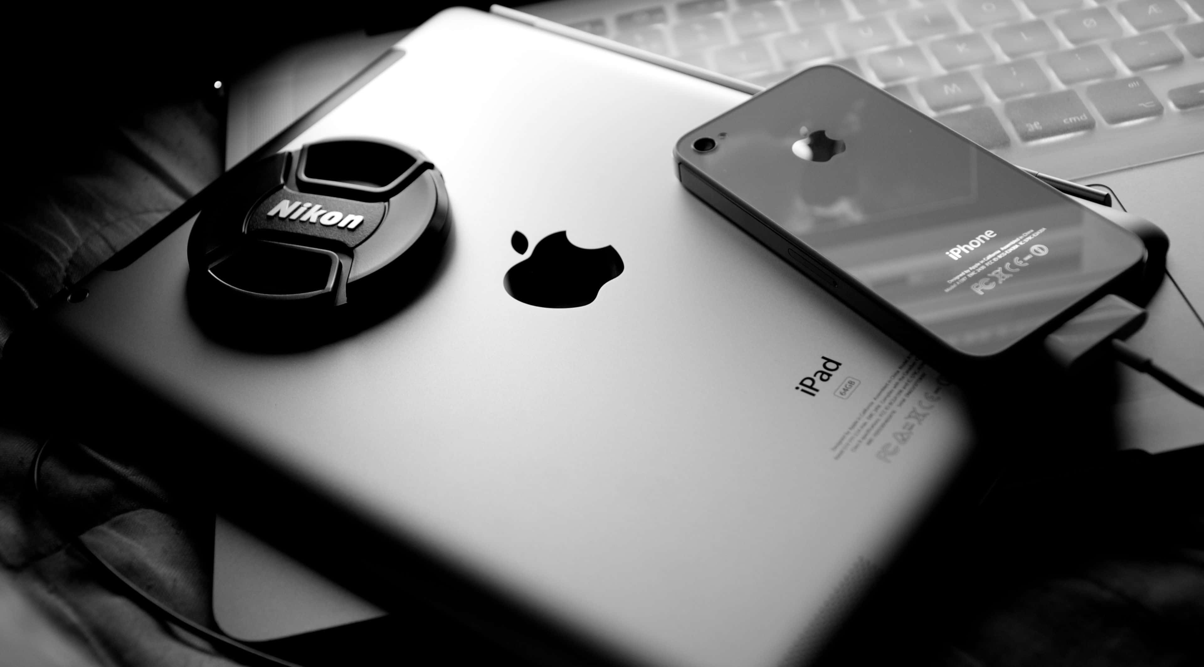4K Apple 桌布 壁紙 — 一個黑白特寫，Nikon鏡頭蓋放在iPad上，旁邊有iPhone，下方是筆記型電腦鍵盤。