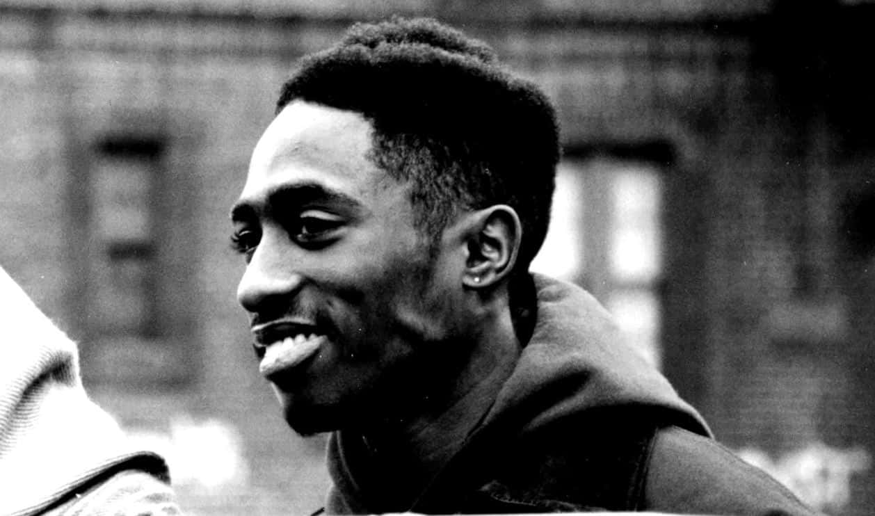 tupac 桌布 壁紙 — 一個黑白特寫，一個微笑的年輕男子穿著連帽衫，背景是模糊的城市建築。