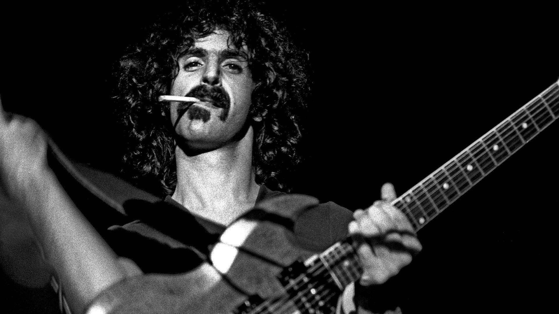 Zappa 桌布 壁紙 — 一個黑白特寫，一個捲髮留鬍子的男人拿著吉他，嘴裡叼著煙。