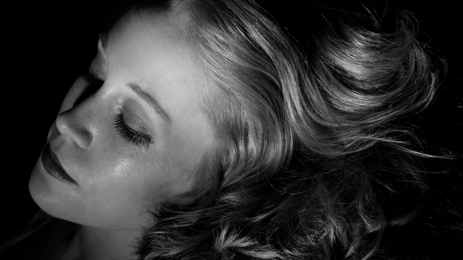 Film Noir 桌布 壁紙 — 一個黑白特寫，女性面孔閉上眼睛，柔和光線，深色背景。