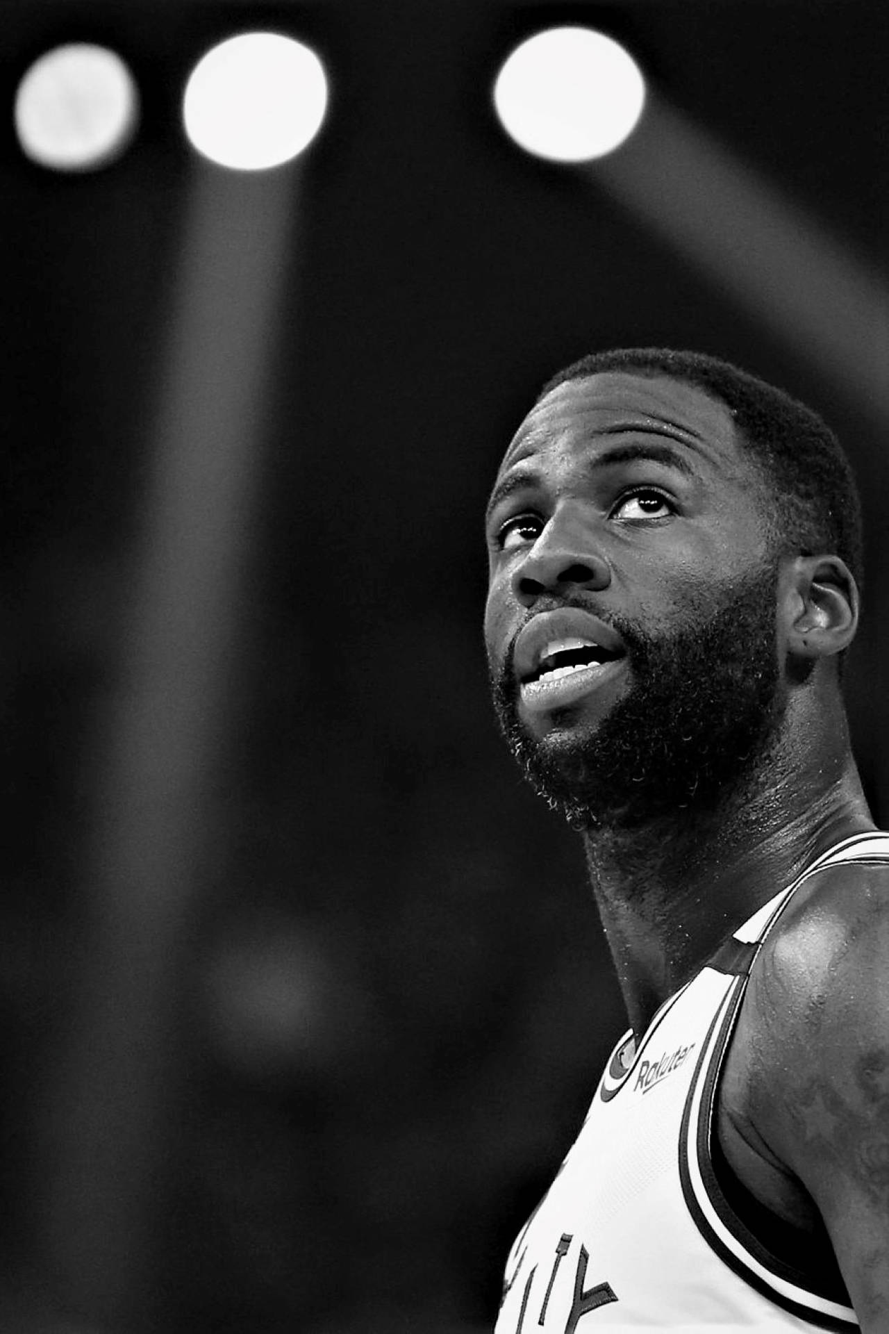 Draymond Green 桌布 壁紙 — 一個黑白特寫，專注的籃球運動員在明亮的場地聚光燈下向上看。