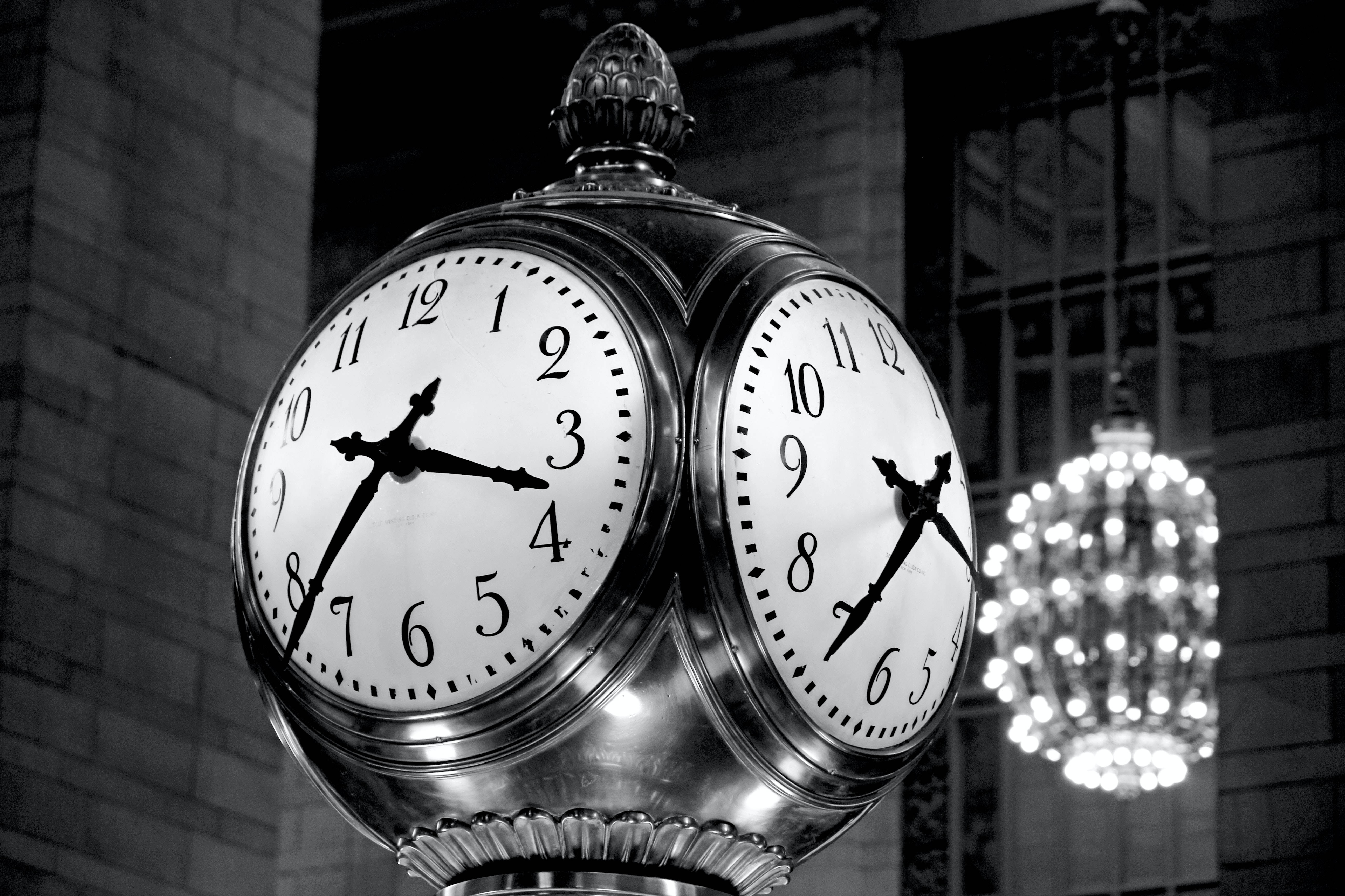 Clock 桌布 壁紙 — 一個黑白特寫的復古雙面時鐘，帶有華麗的金屬工藝和背景中發光的水晶吊燈。