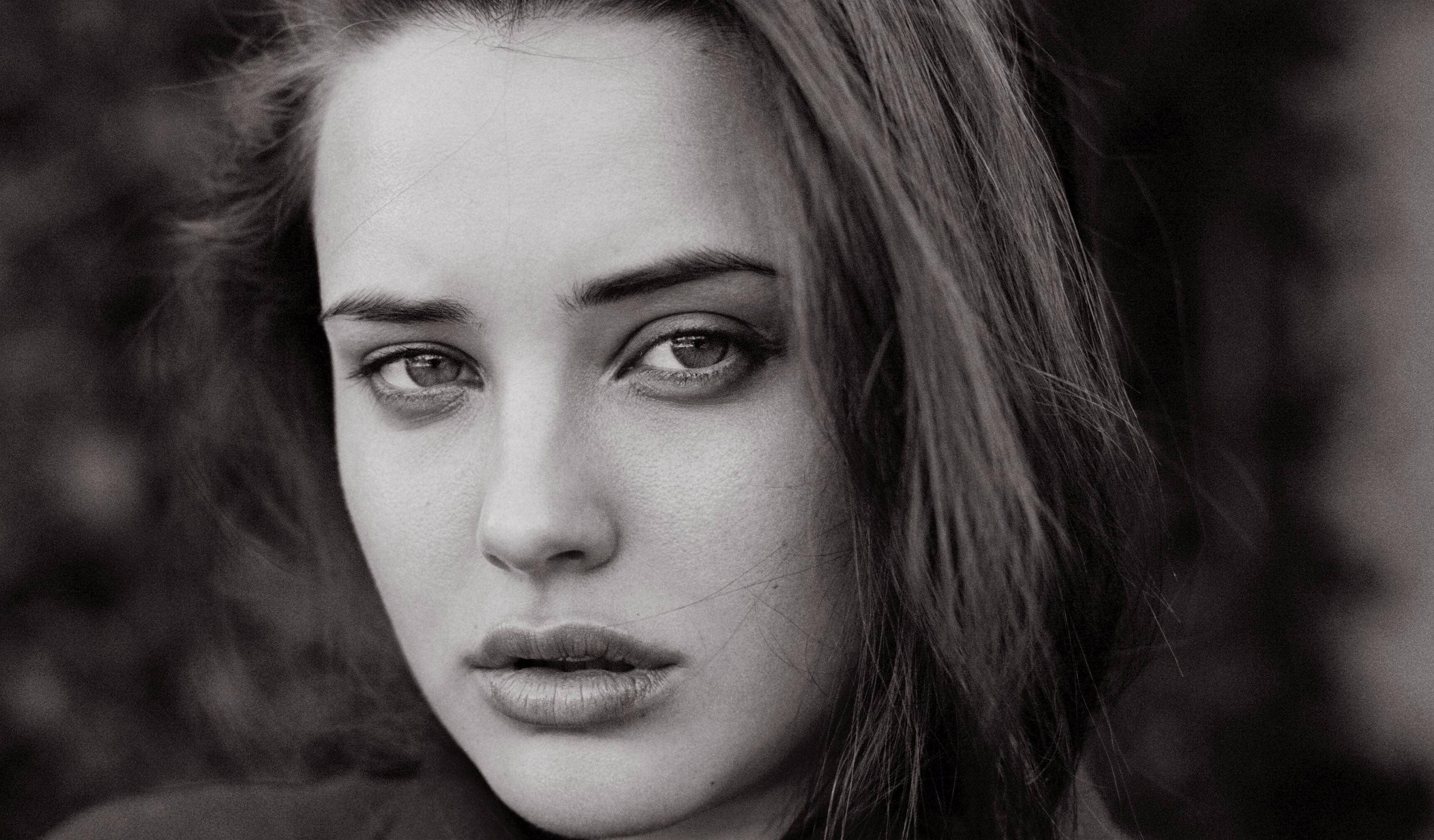 Katherine Langford 桌布 壁紙 — 一個黑白特寫肖像，一位眼神強烈、頭髮柔軟的女性，臉龐在模糊背景襯托下。