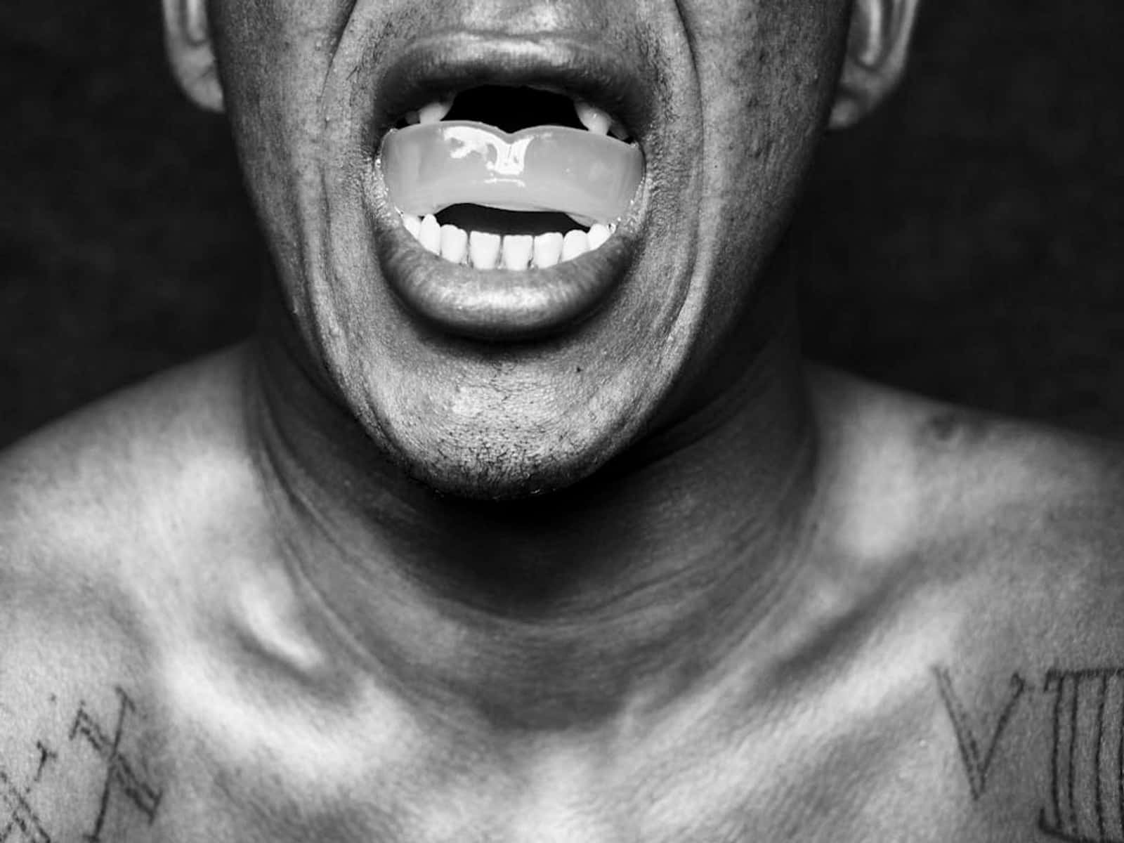 運動 桌布 壁紙 — 一個黑白特寫鏡頭，展示一名男子張開的嘴巴，露出牙齒矯正器和肩膀上的刺青。