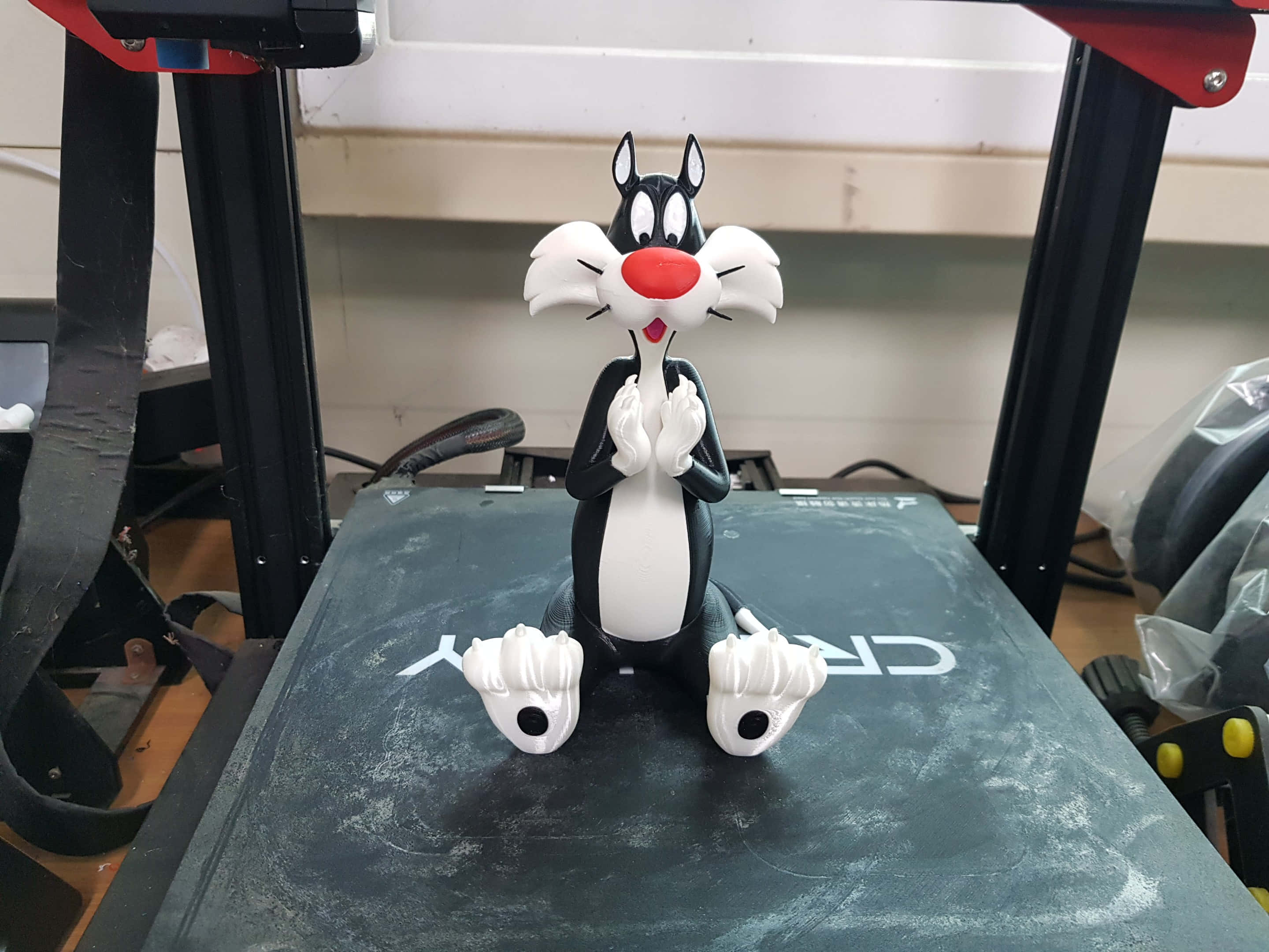 Sylvester The Cat 桌布 壁紙 — 一個黑白相間的 Sylvester the Cat 公仔，雙手合攏，雙腳張開，坐在深灰色表面上，周圍是工作室設備。