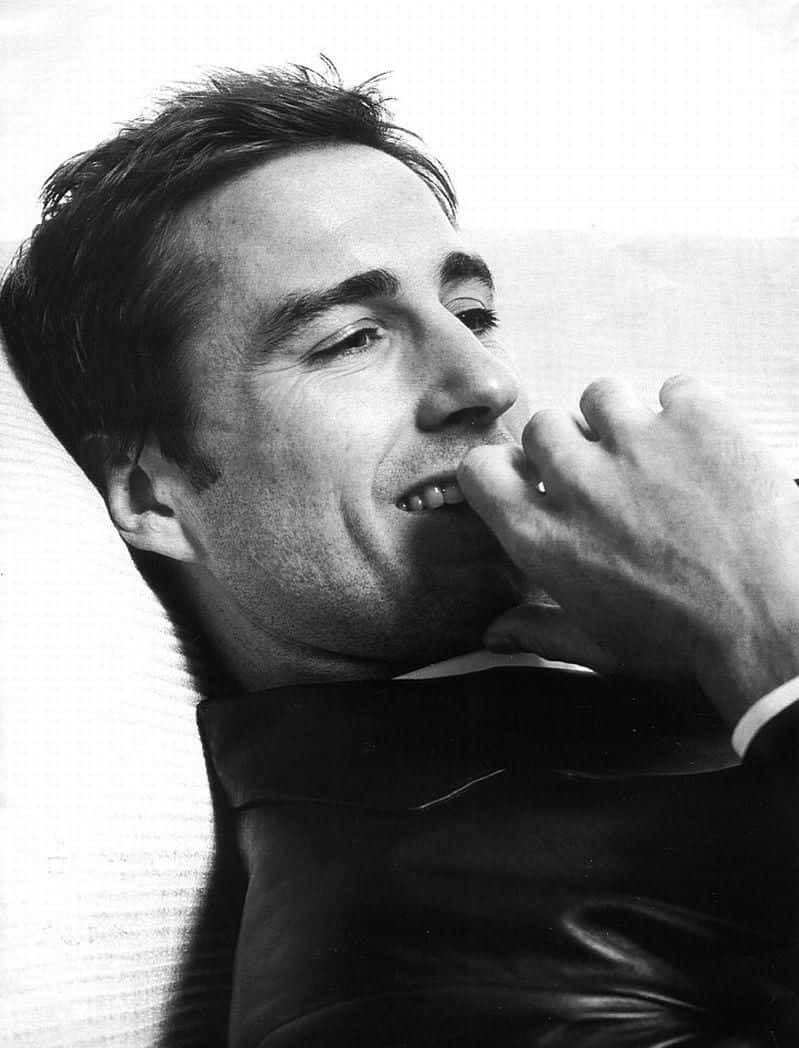 Luke Wilson 桌布 壁紙 — 一個黑白相間的男人向後靠，手靠近嘴邊，眼睛向上凝視，呈現沉思姿態。