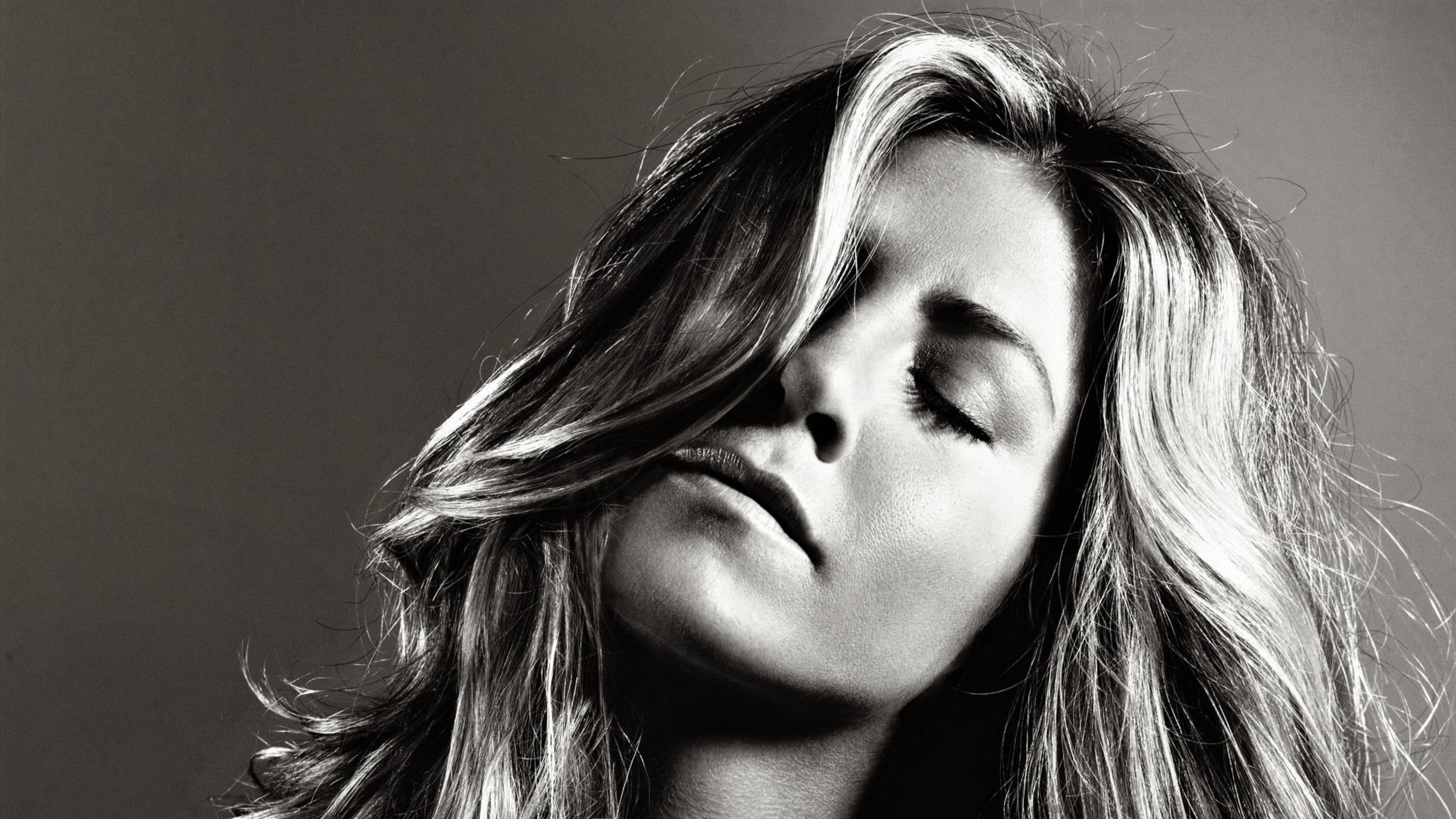 Jennifer Aniston 桌布 壁紙 — 一個黑白肖像，一位女性閉上眼睛，頭髮飄逸，背景簡潔。