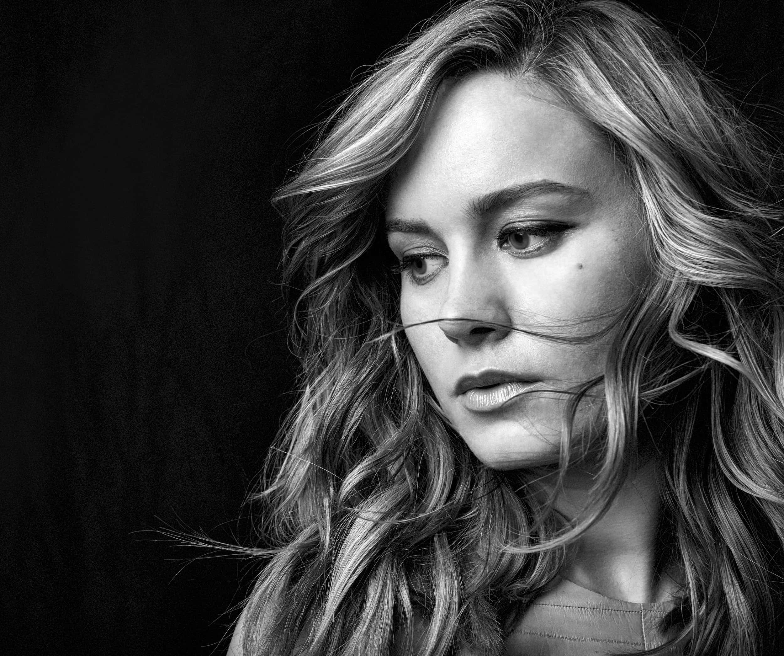 brie larson 桌布 壁紙 — 一個黑白肖像，一位波浪髮型的女性在深色背景下向下看。