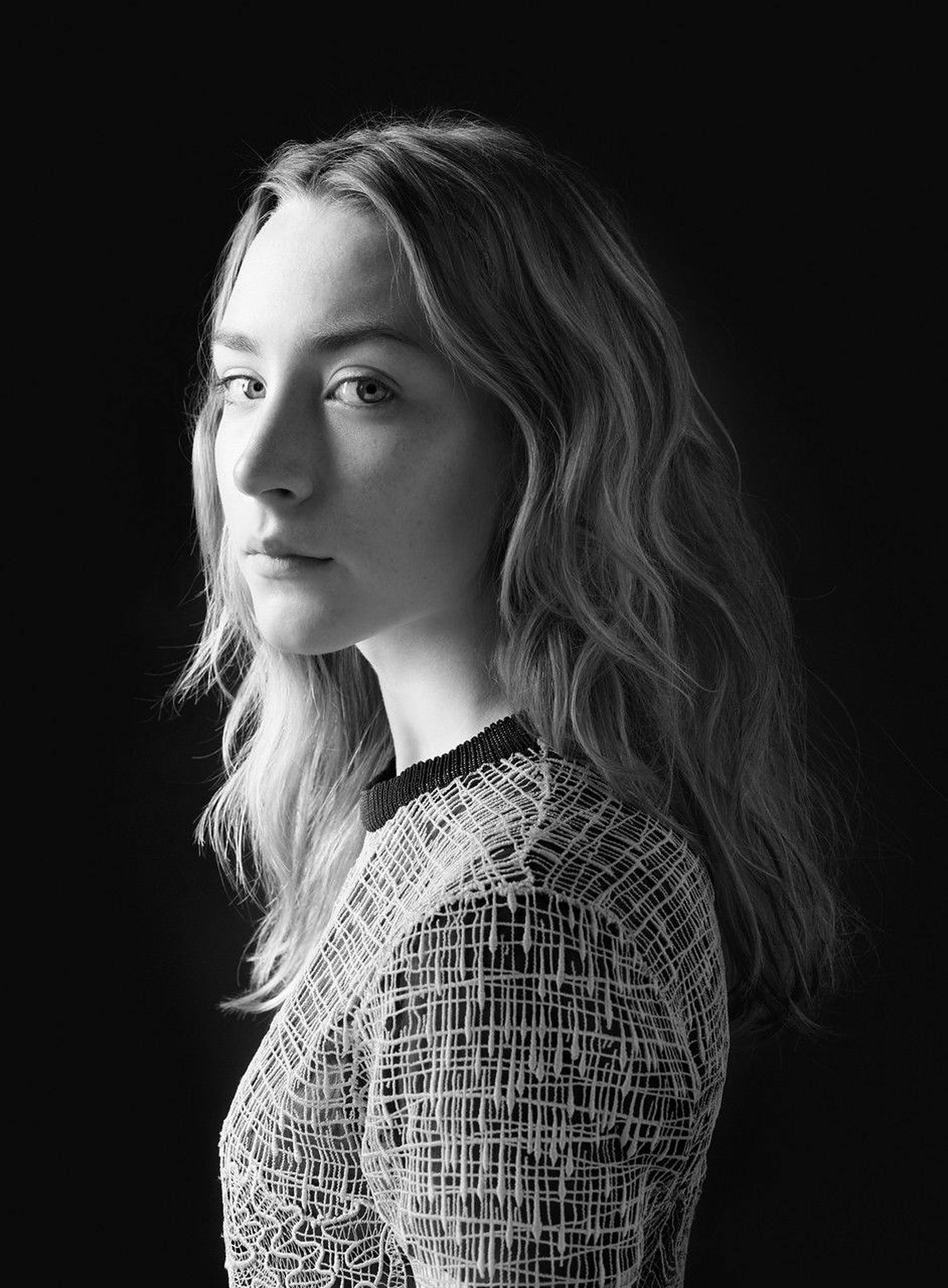 Saoirse Ronan 桌布 壁紙 — 一個黑白肖像，一位波浪髮女性穿著質感上衣，背景深色。
