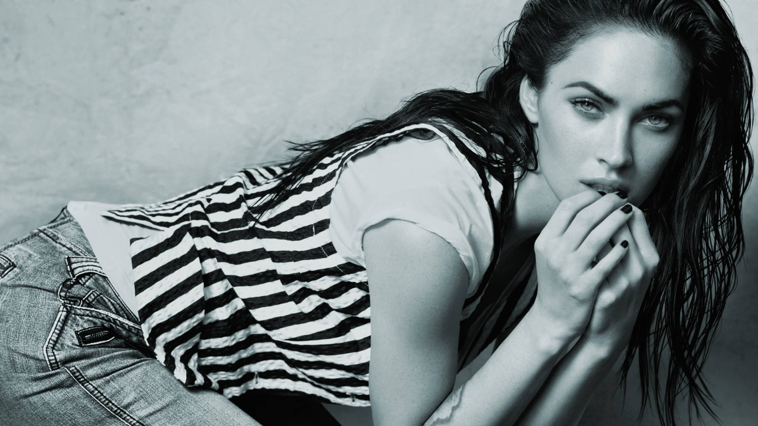 Megan Fox 桌布 壁紙 — 一個黑白肖像，一位濕髮和深色指甲的女性將下巴擱在手上，靠著紋理牆壁。