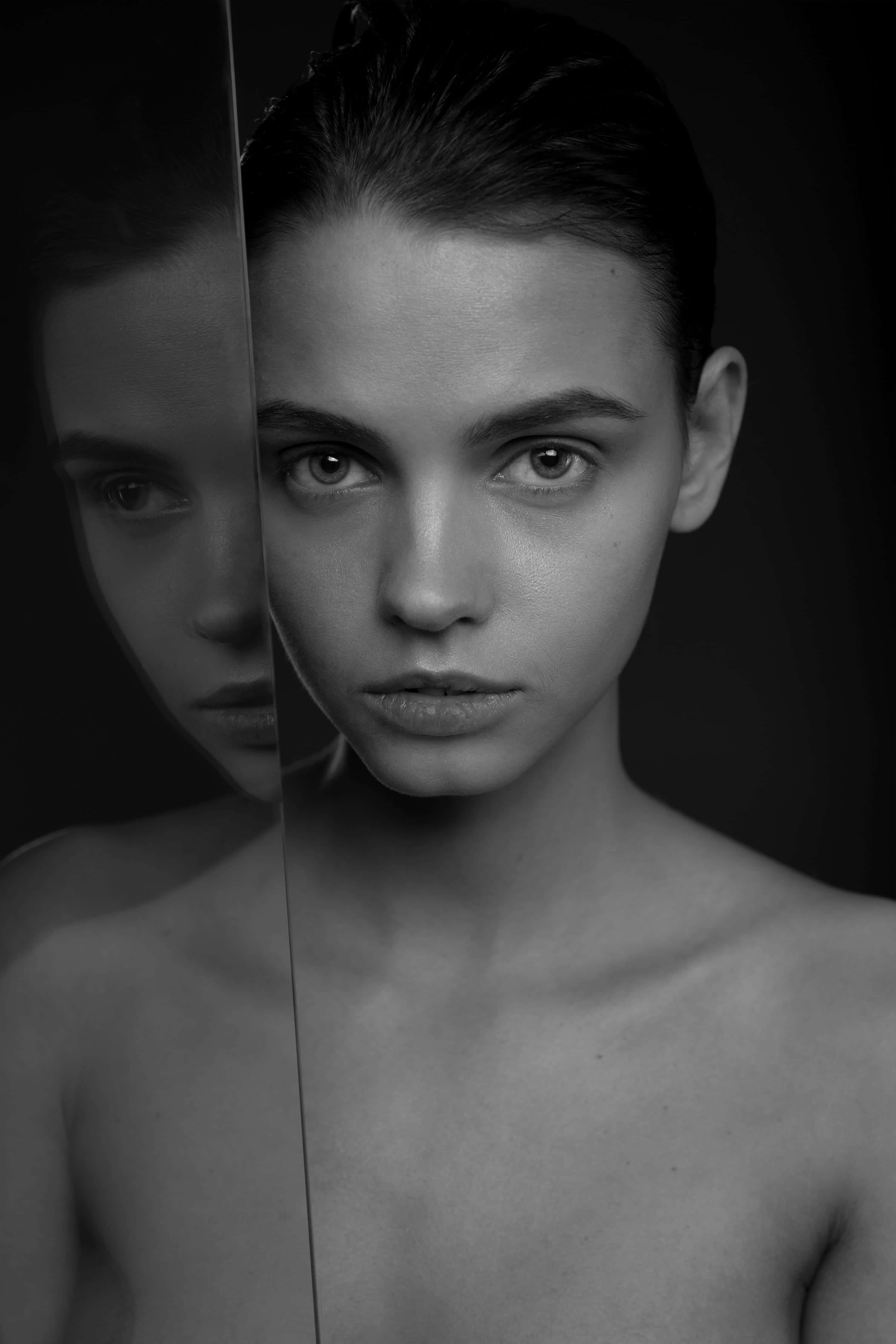 Black And White Fashion 桌布 壁紙 — 一個黑白肖像，一位眼神強烈的女性被垂直鏡面反射在黑暗背景上分割。