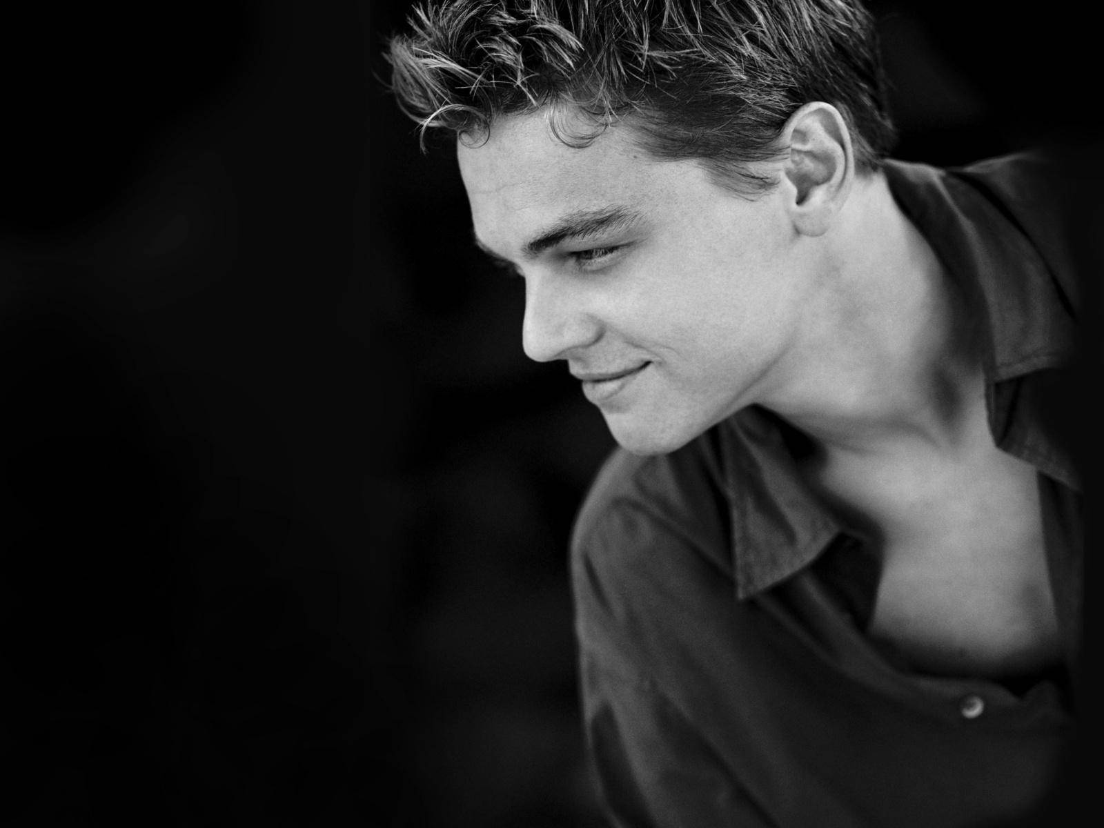 Dicaprio 桌布 壁紙 — 一個黑白肖像，一個年輕男子頭髮蓬亂，低頭微笑，背景深色。