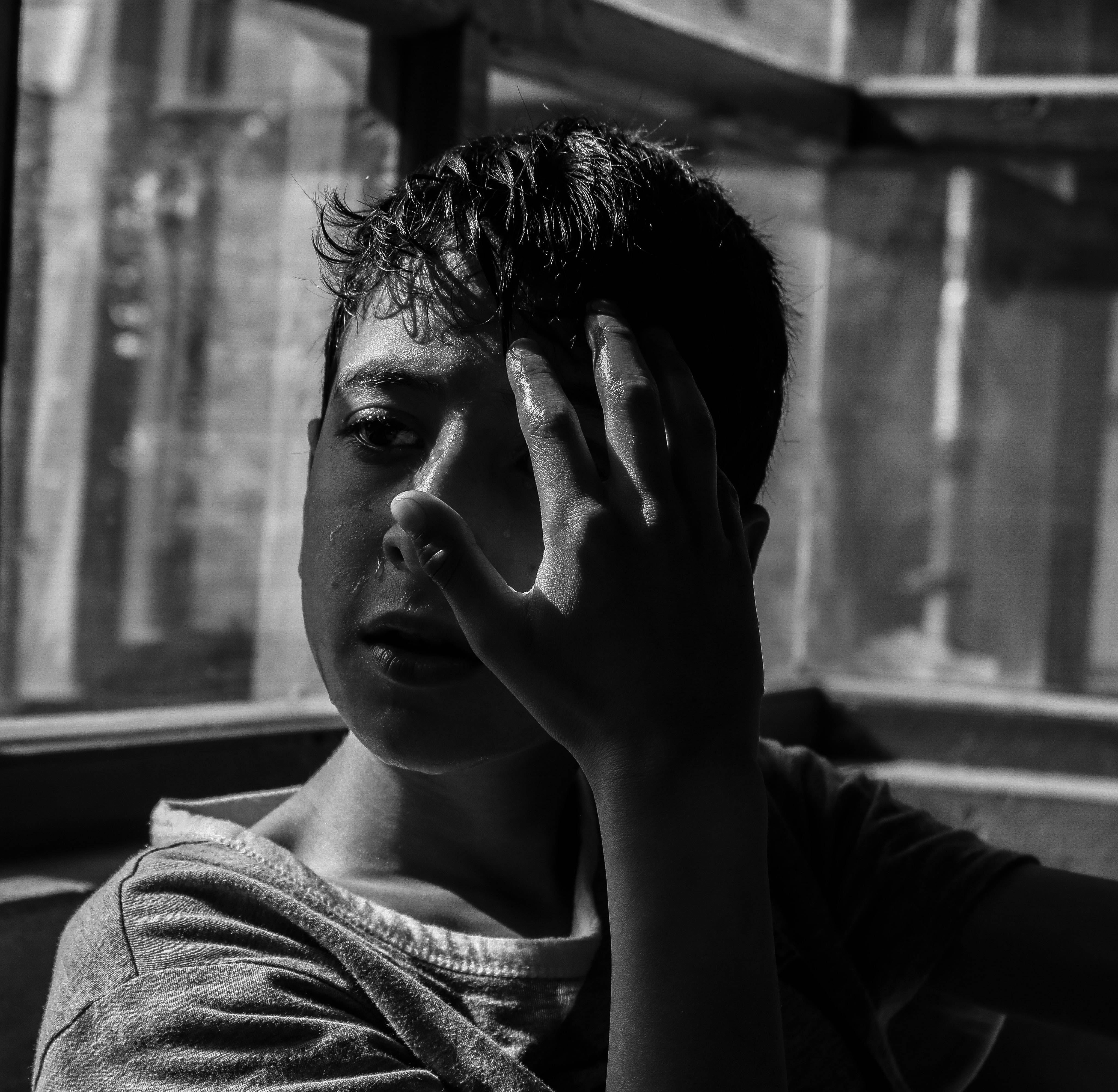 crying sad boy 桌布 壁紙 — 一個黑白肖像，一個年輕男孩臉上掛著淚水，用手遮住眼睛，靠近窗戶。